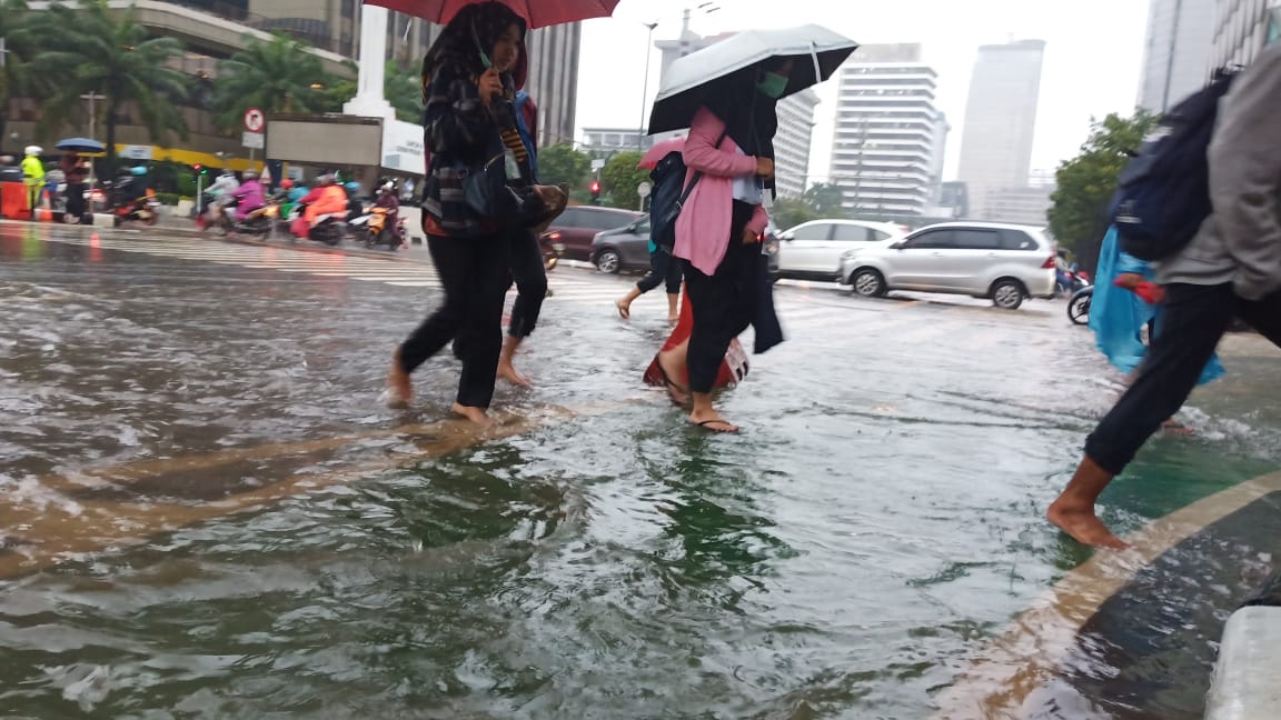 Karyawan menyeberangi Jalan Thamrin yang tergenang, Selasa (25/2).