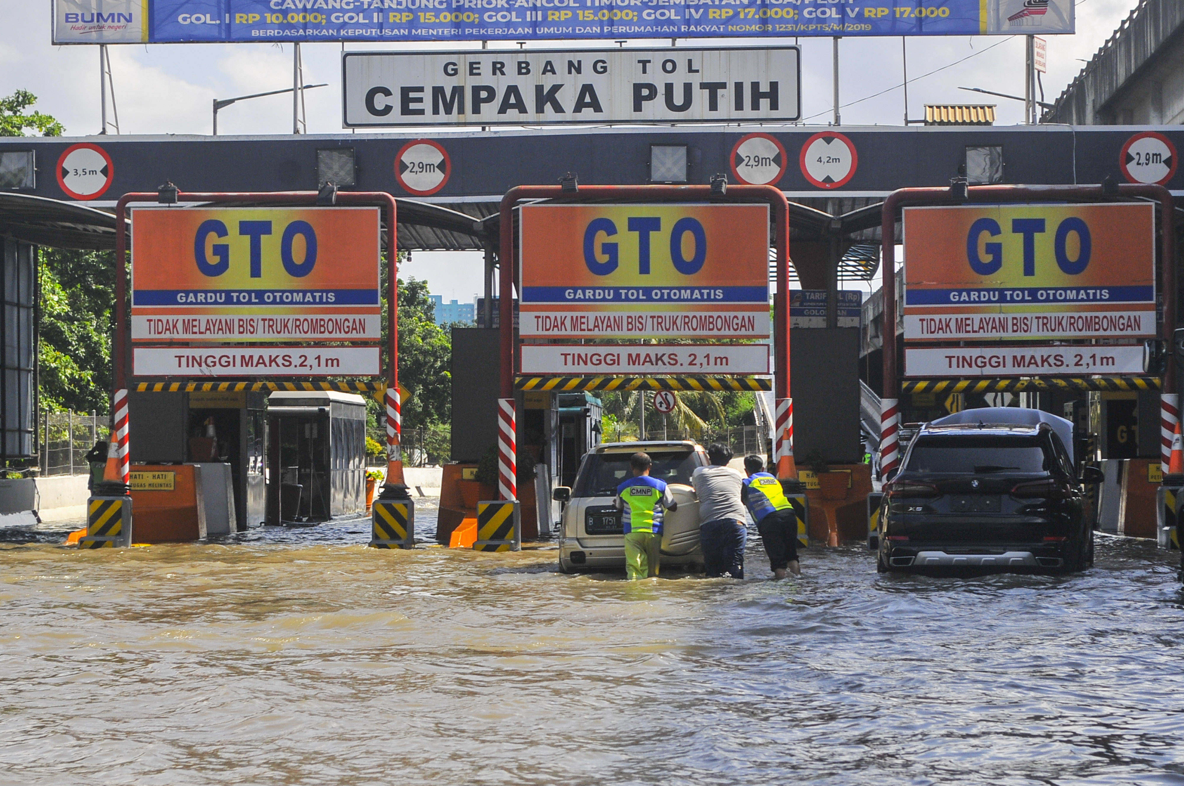 Sejumlah petugas membantu mendorong mobil yang mogok akibat banjir di gerbang tol Cempaka Putih, Jakarta Pusat, Minggu (23/2).