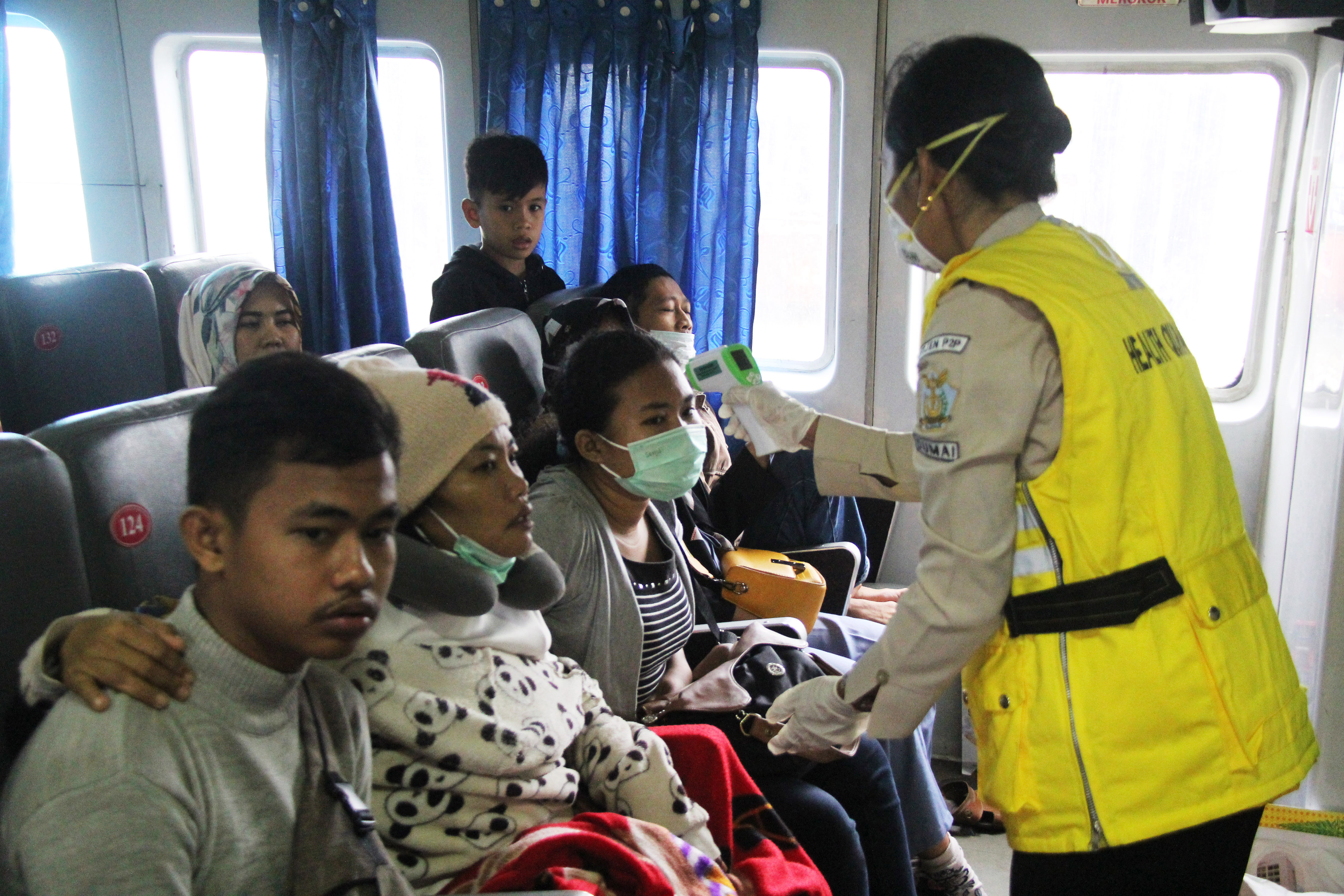 Seorang Petugas medis (kanan) memeriksa suhu tubuh penumpang menggunakan thermometer non kontak di dalam kapal yang baru tiba dari Melaka.