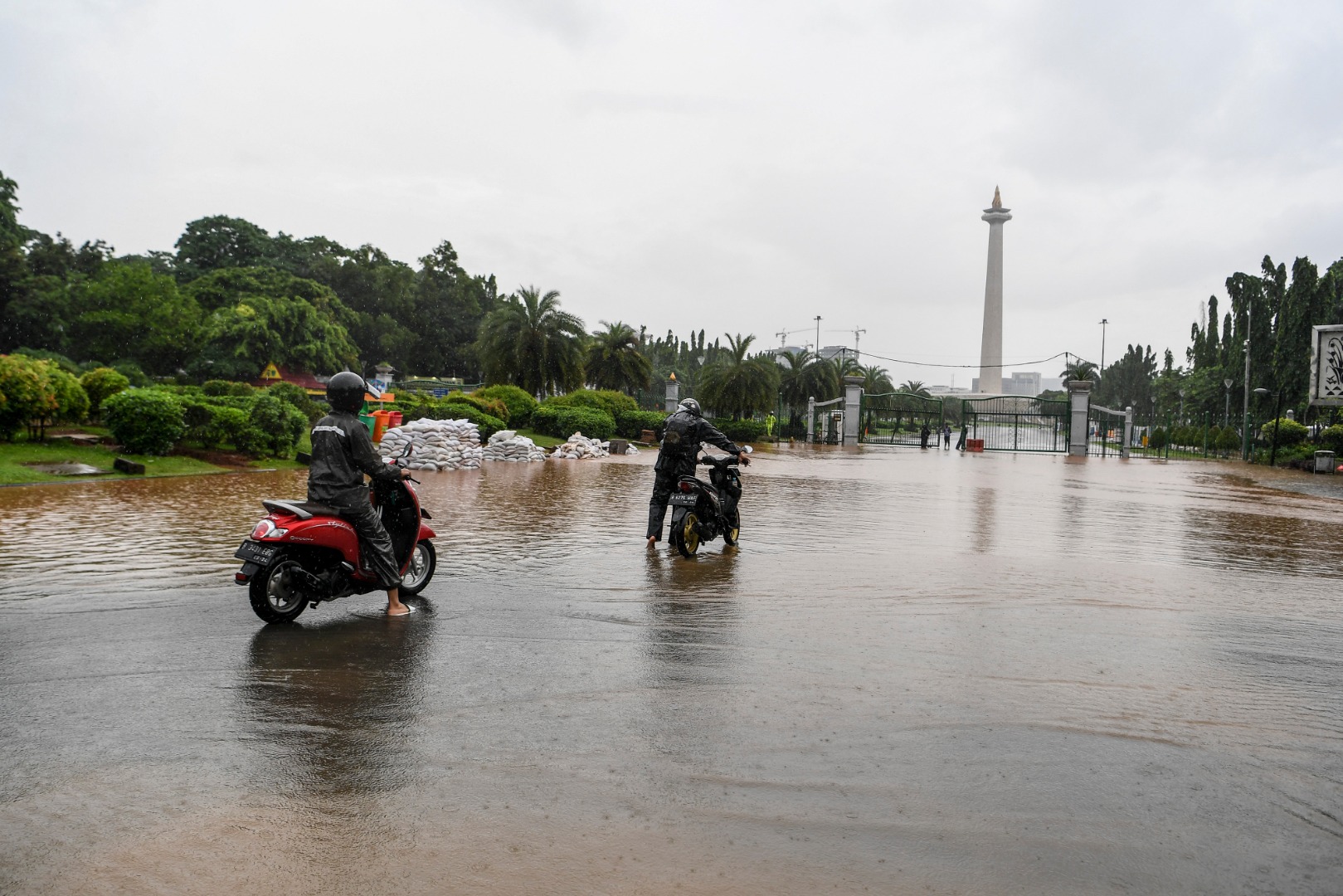 Warga mendorong motor melintasi banjir di kawasan Monas, Jalan Medan Merdeka Barat, Jakarta.