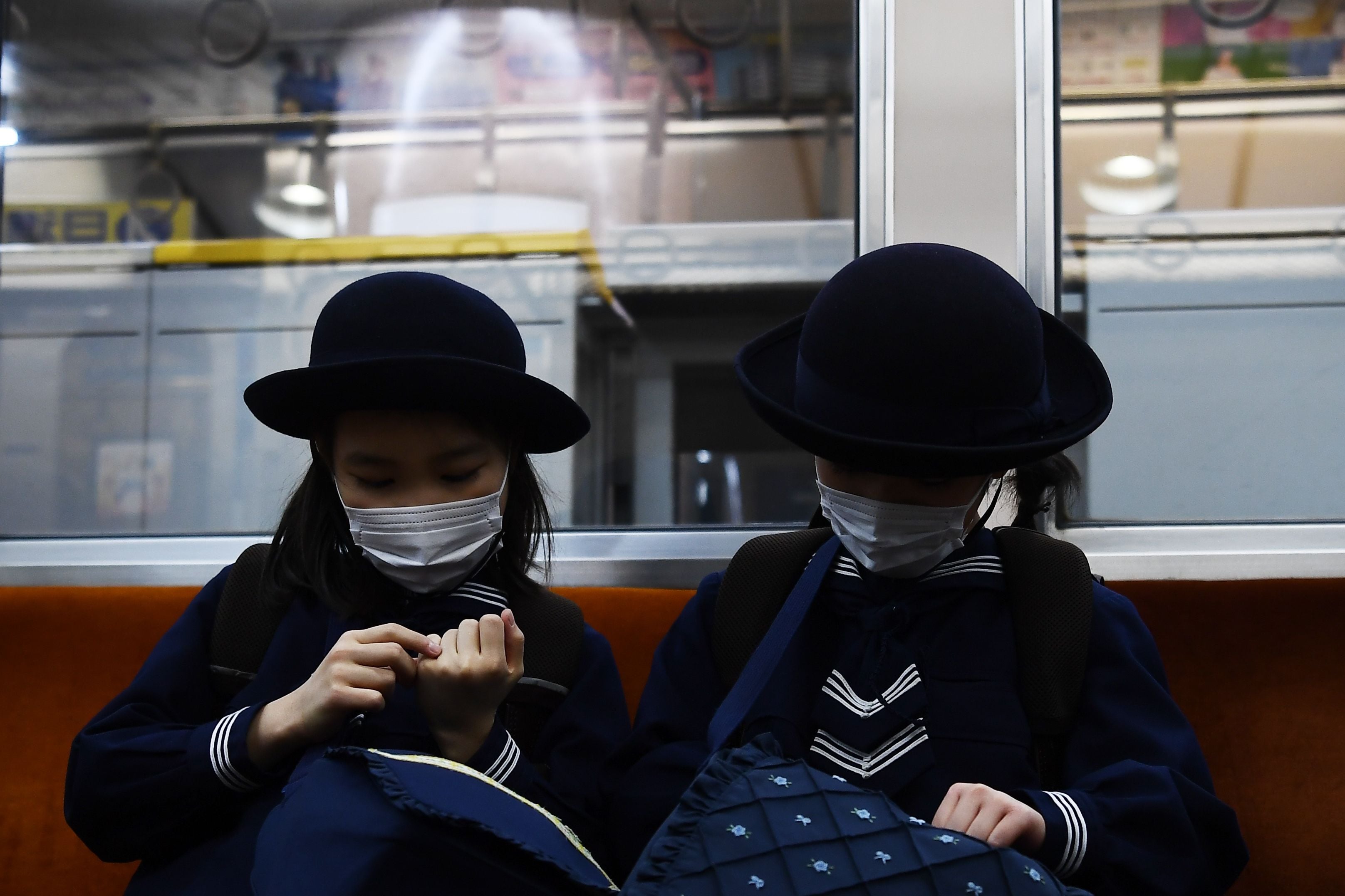 Dua pelajar putri mengenakan masker saat menumpang kereta di Tokyo, Jepang.