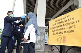 Seorang pegawai tengah diperiksa suhu tubuhnya saat hendak masuk kantor.