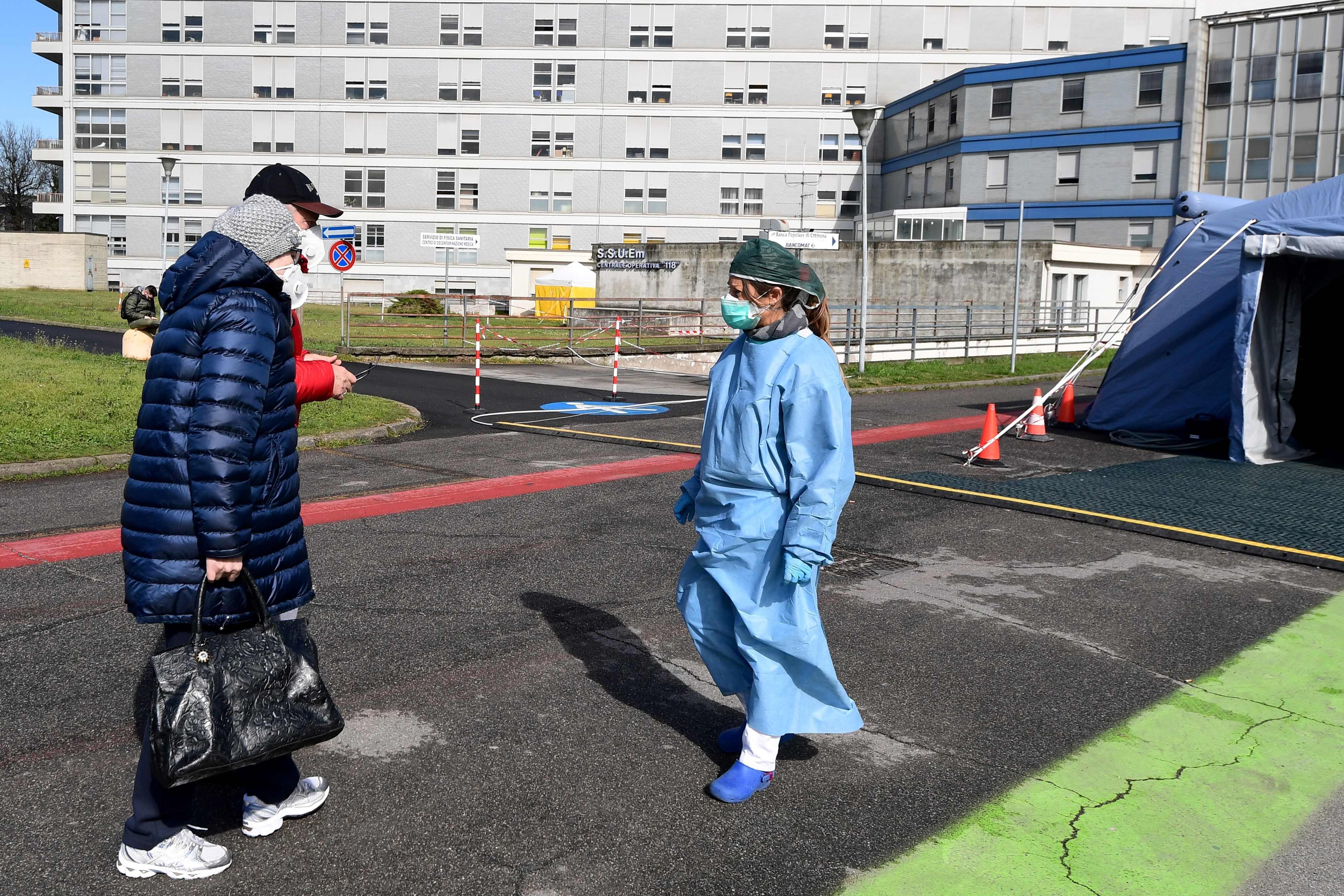 Dua warga disambut seorang petugas kesehatan di depan tenda darurat yang berada di depan rumah sakit Cremona, Italia.