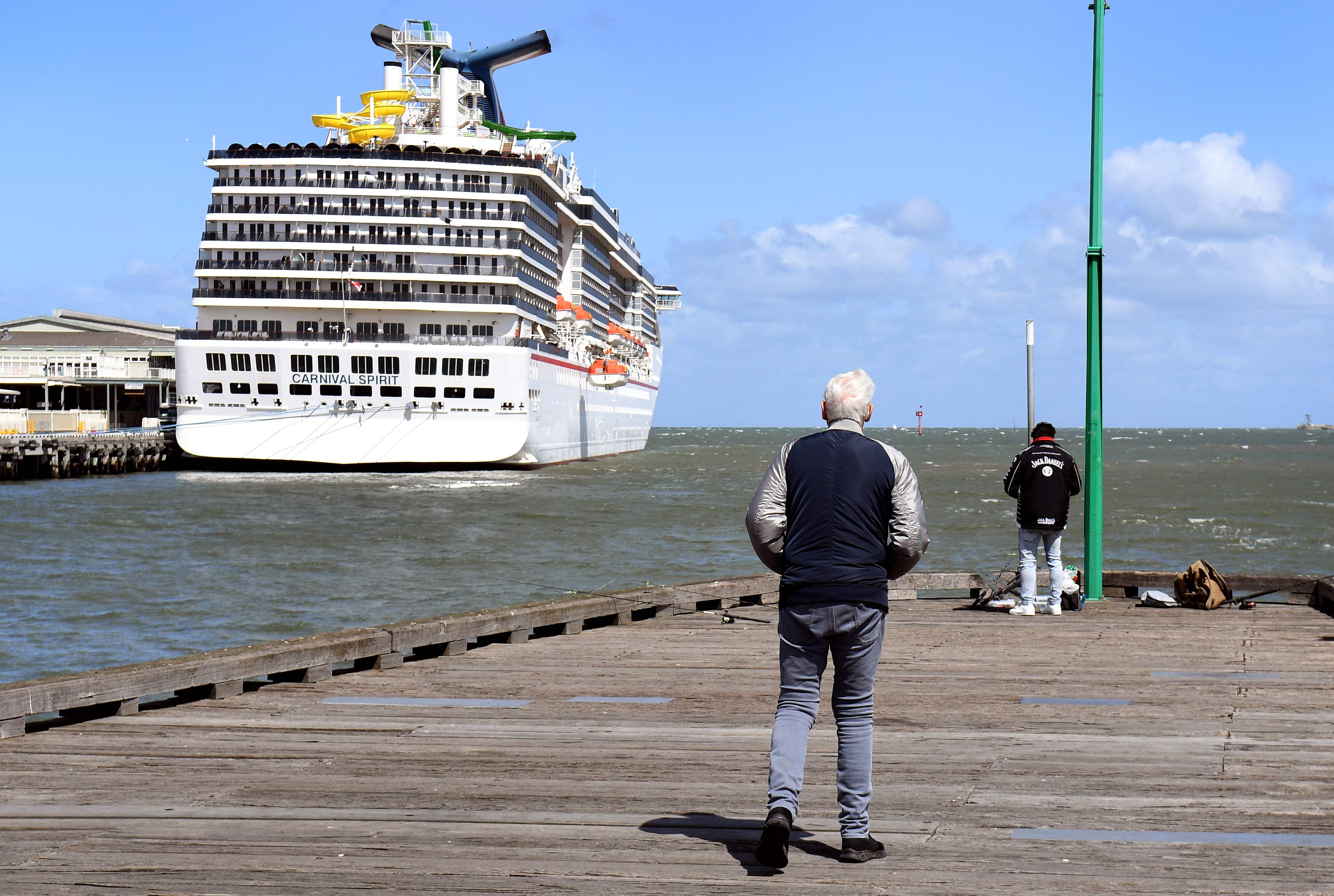 Seorang pria berdiri di pelabuhan Melbourne melihat kapal pesiar yang sedang berlabuh.