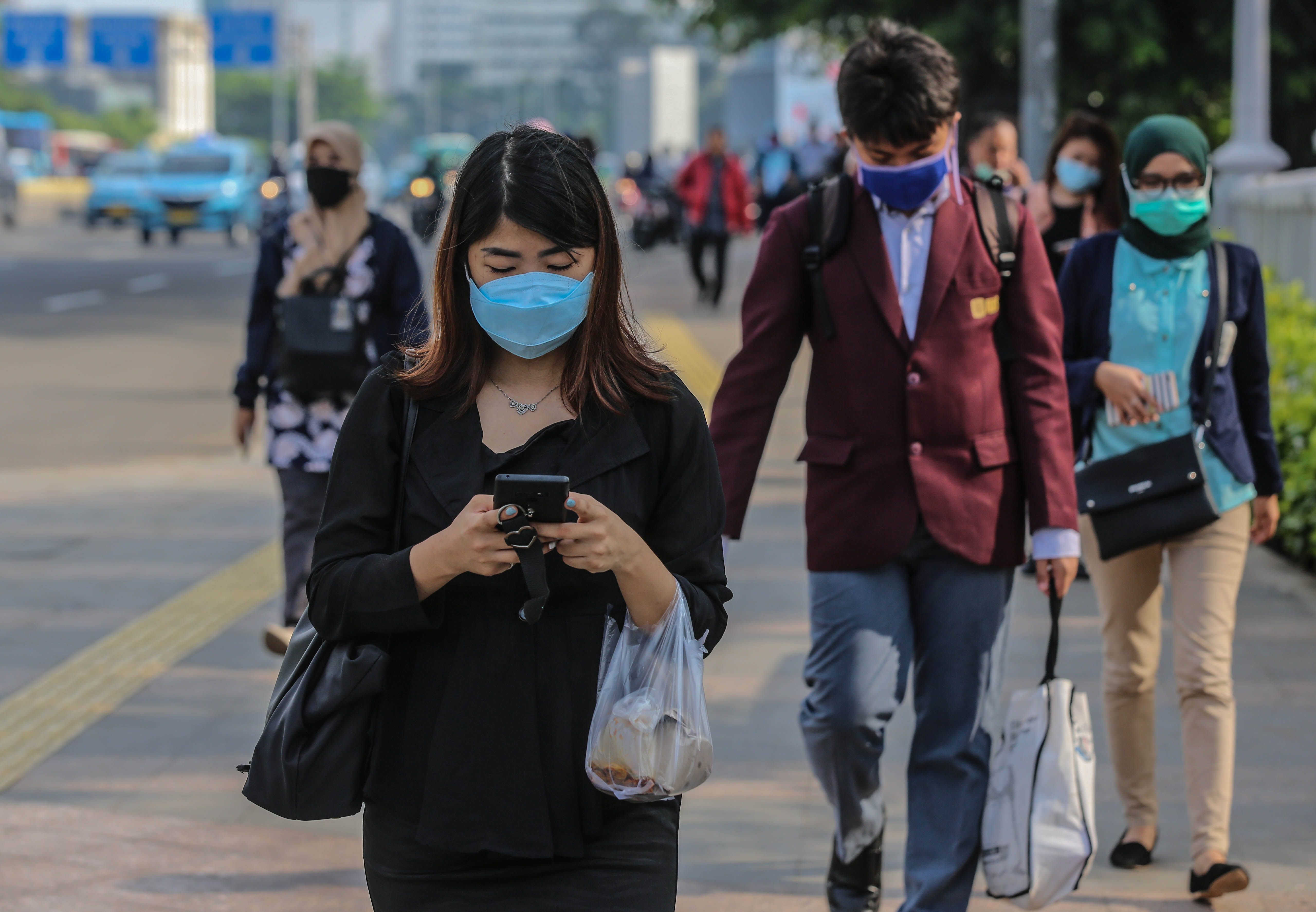 Pekerja menggunakan masker pelindung saat melewati trotoar menuju kantornya di kawasan Sudirman, Jakarta, Selasa (3/3/2020).