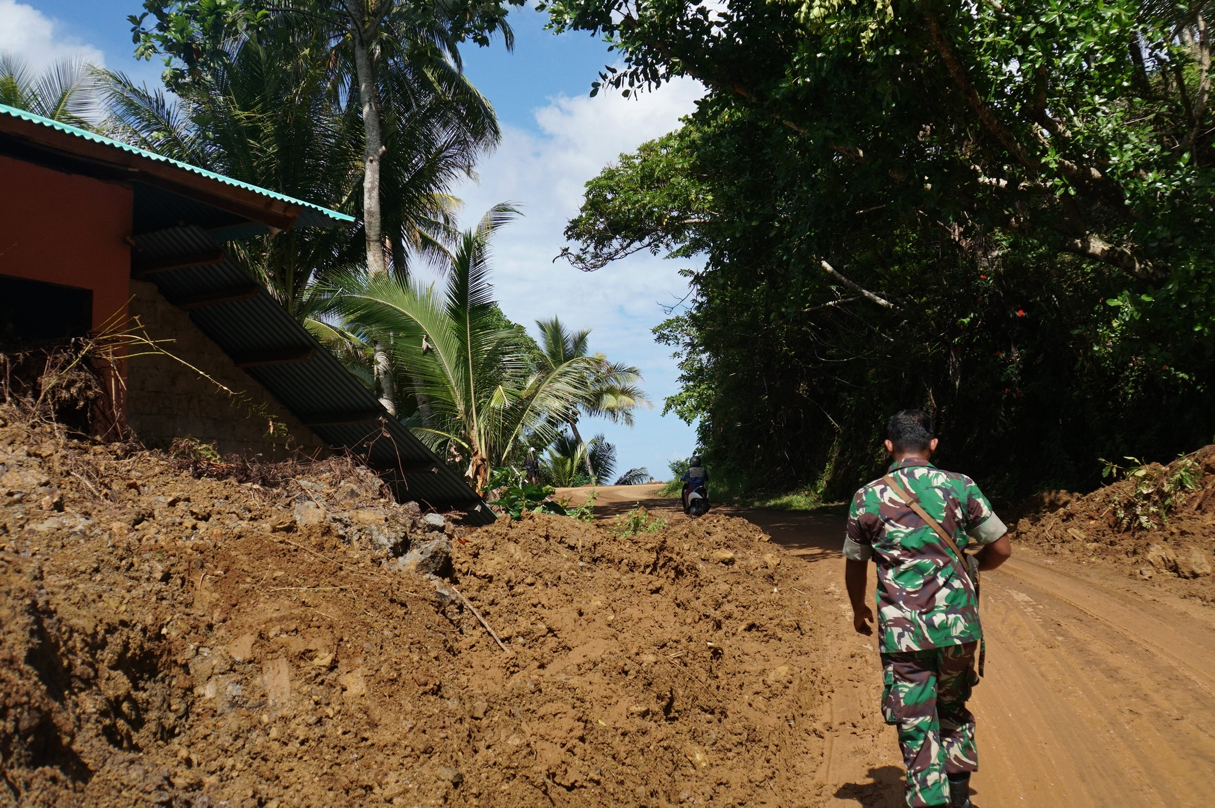  Anggota TNI berjalan di lokasi permukiman yang tertutup material tanah akibat banjir bandang di Desa Lebo, Manganitu, Sulawesi Utara.
