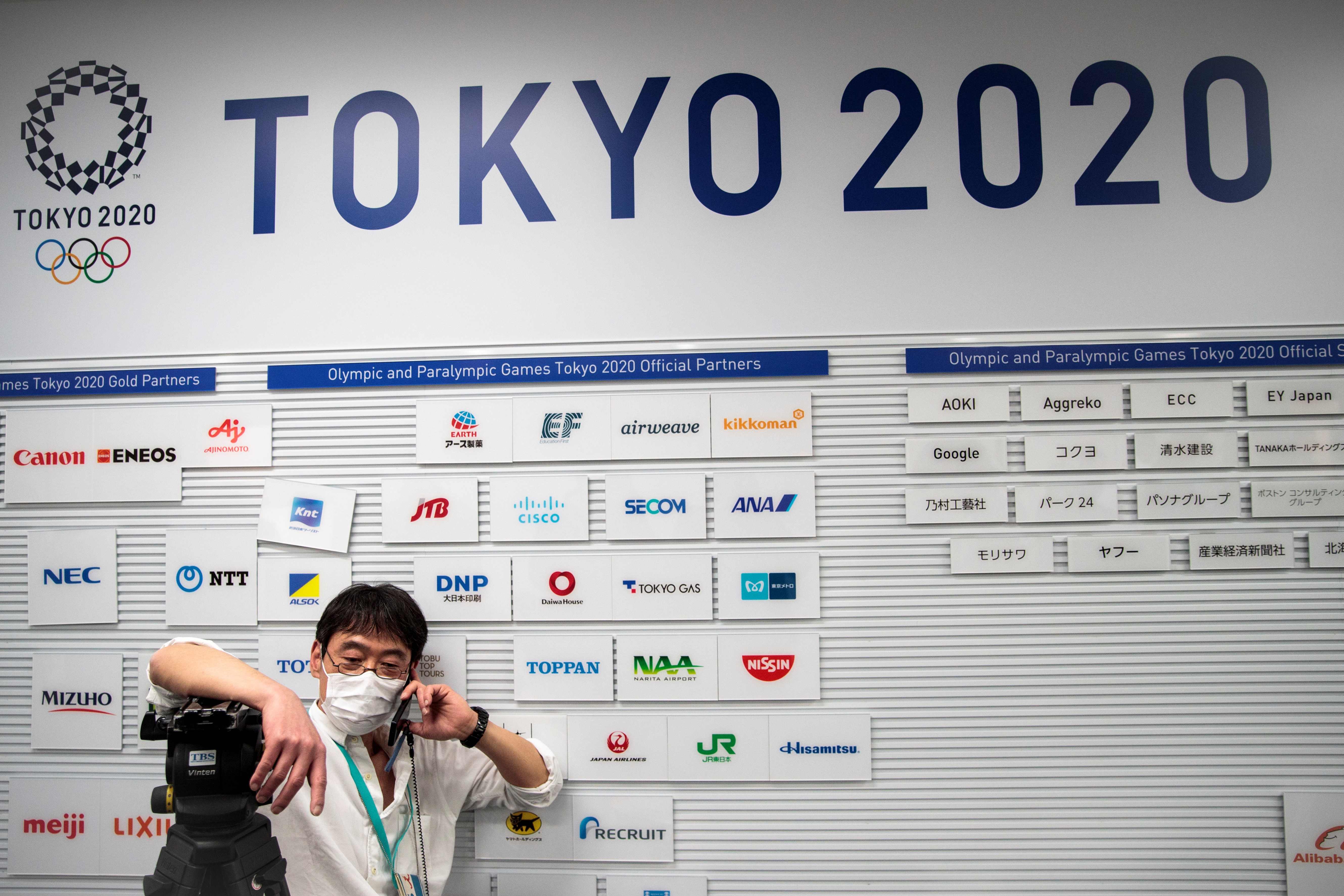 Seorang jurnalis berdiri di depan papan bertuliskan Olimpiade Tokyo 2020