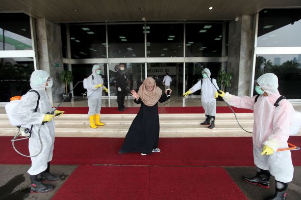 Petugas melakukan penyemprotan cairan disinfektan kepada setiap pengunjung yang datang di depan lobby gedung Nusantara III DPR.