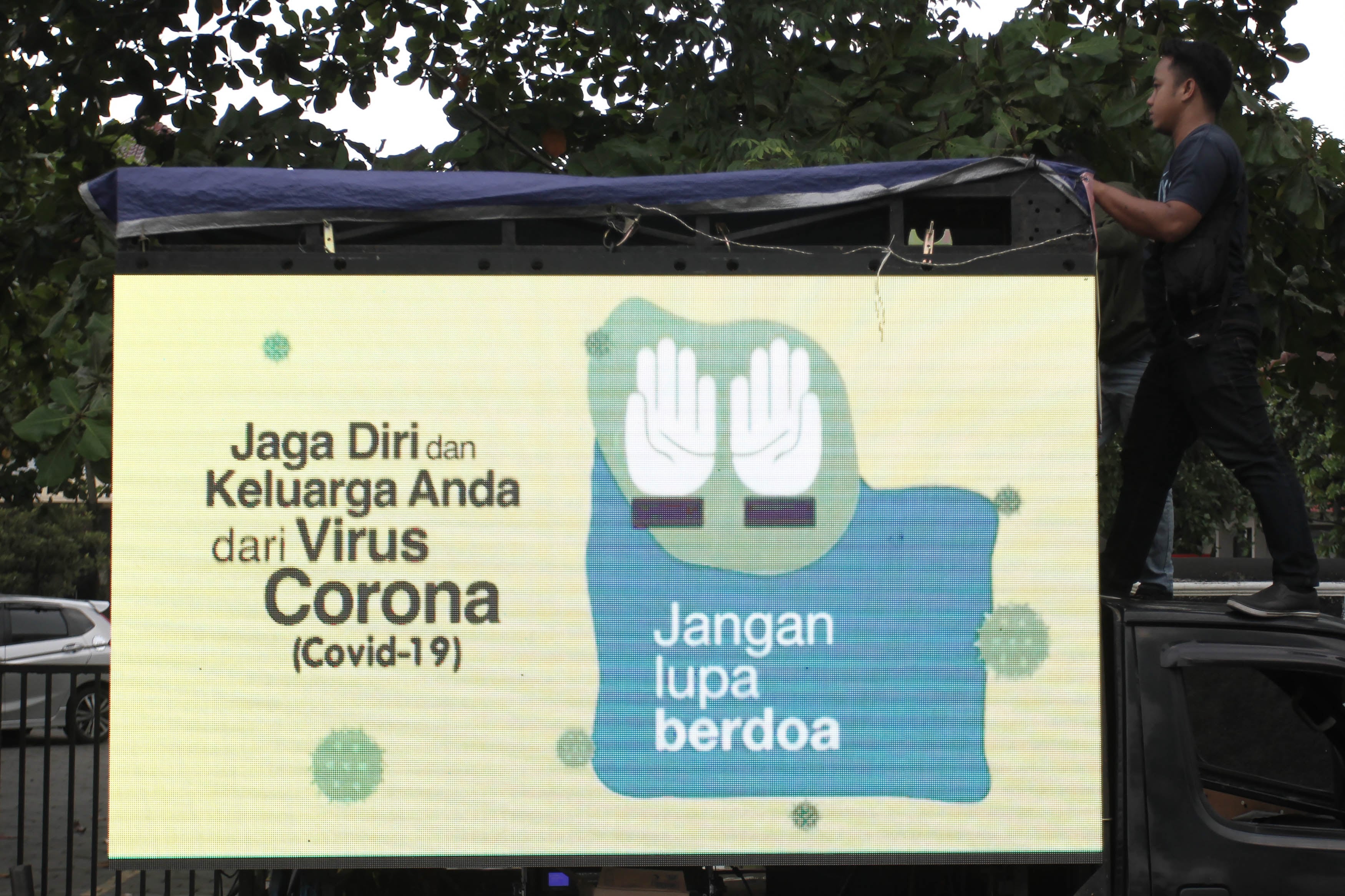 Pekerja memasang terpal pada layar monitor imbauan masyarakat di Yogyakarta.