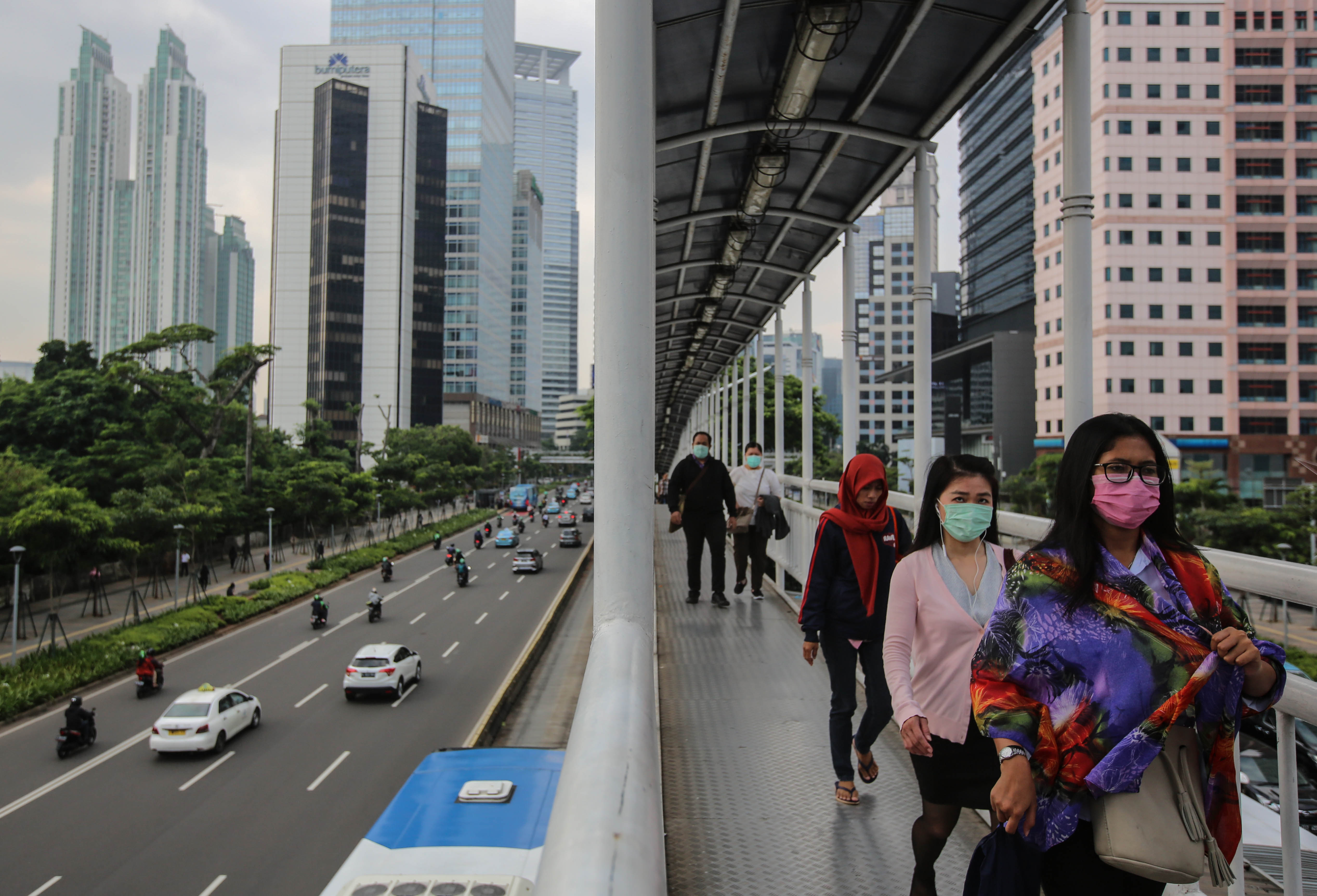 Pekerja menggunakan masker saat melewati jembatan penyeberangan yang terkoneksi halte bus Transjakarta.
