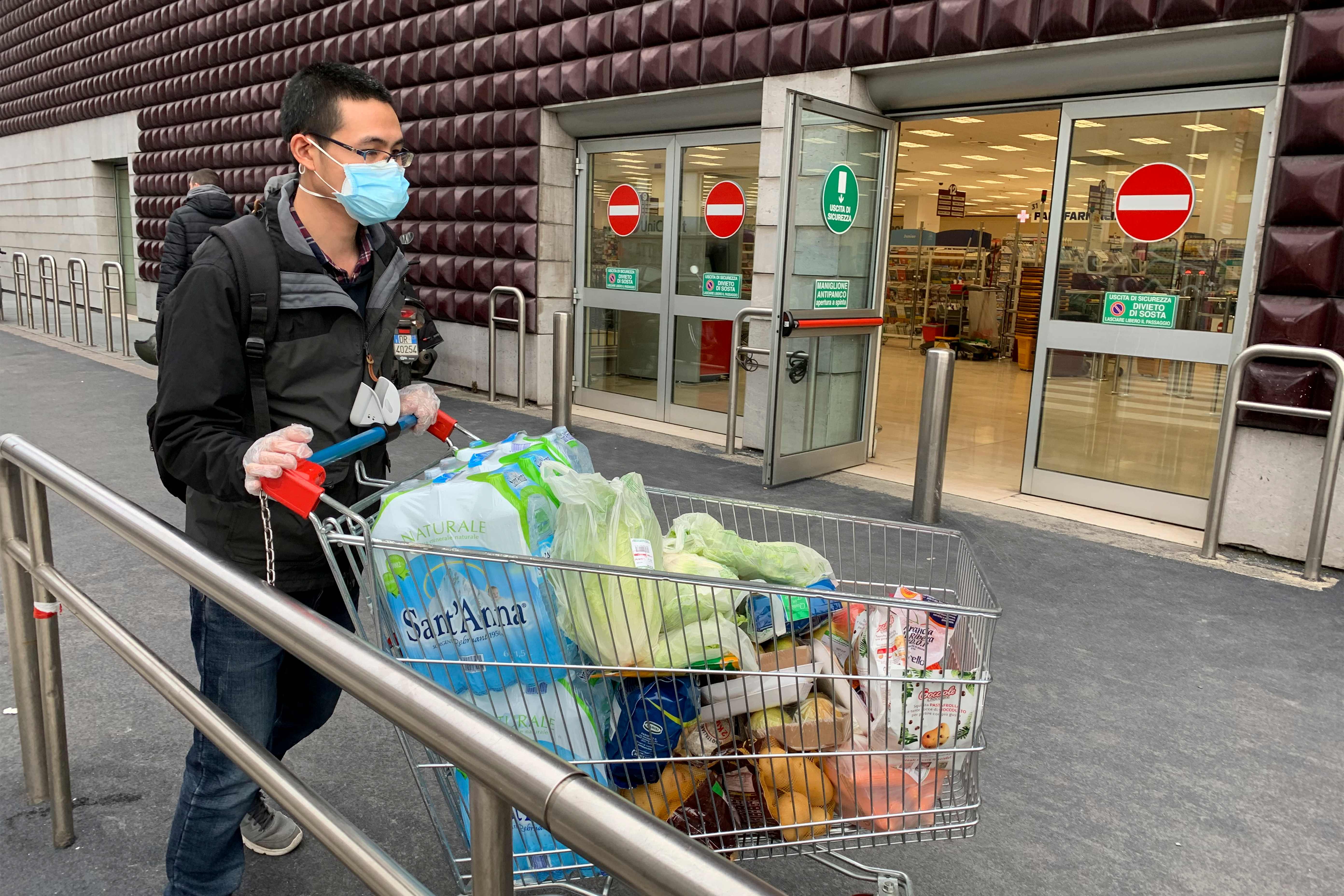  Seorang pria yang menggunakan masker meninggalkan supermarket dengan troli penuh belajaan di Milan, Italia, Minggu (8/2).