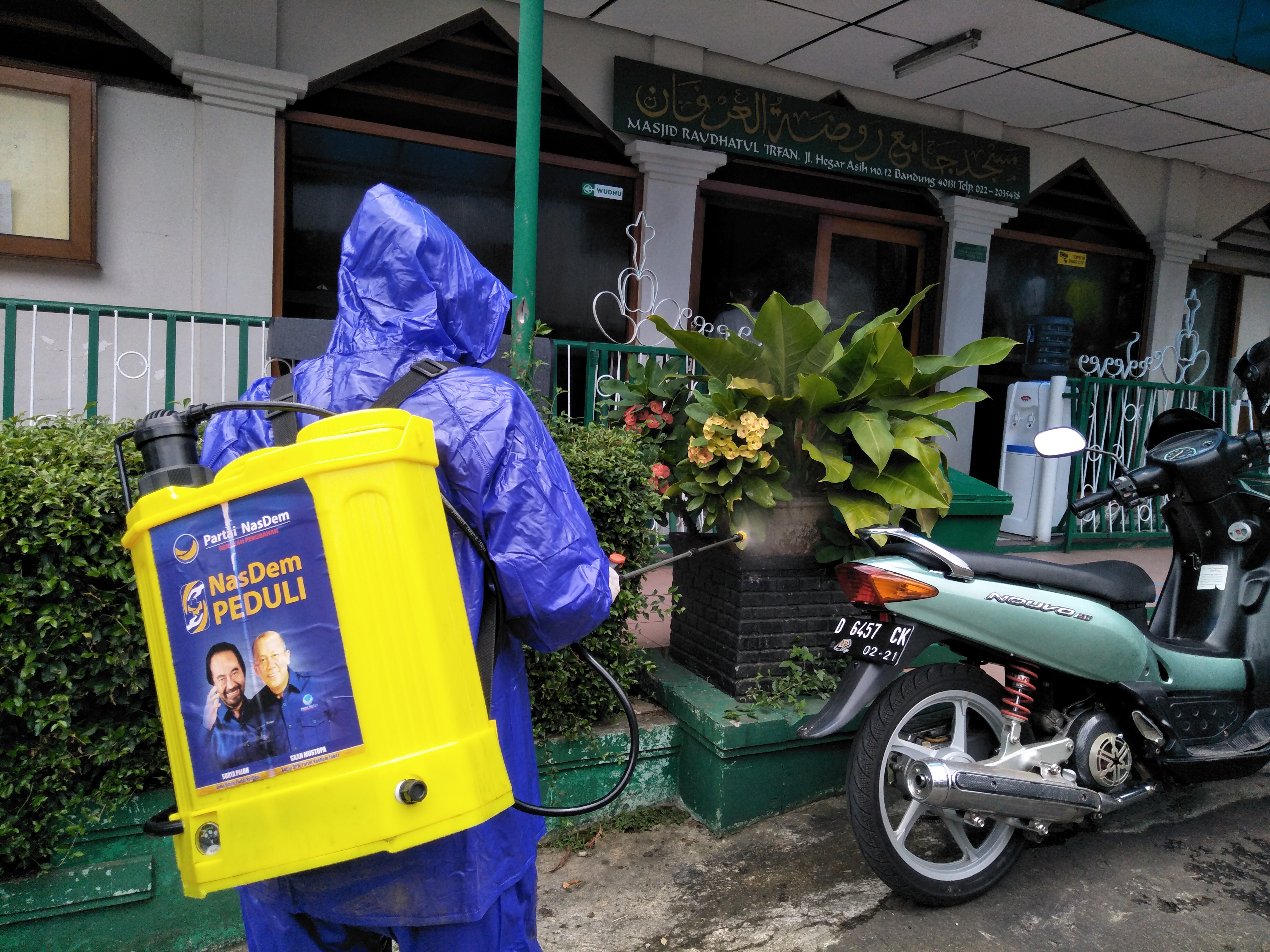 Kader nasdem dibantu petugas menyemprotkan disinfektan di masjid dansekolah luar biasa di kawasan jalan cipaganti, kota bandung