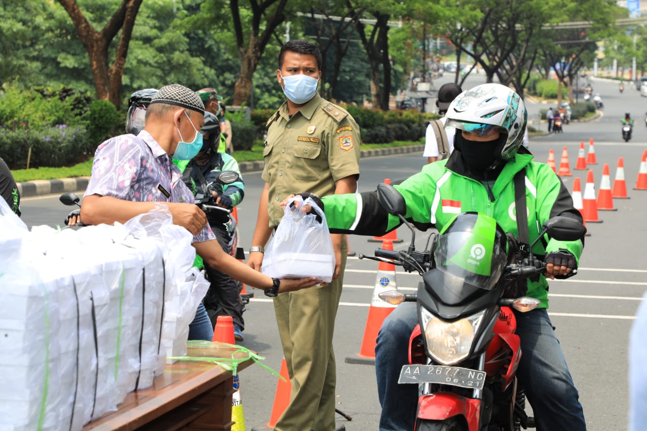 Seorang petugas membagikan nasi kotak kepada driver ojol,  di depan gerbang Kantor Pemprov Jateng, Selasa (31/3/2020).