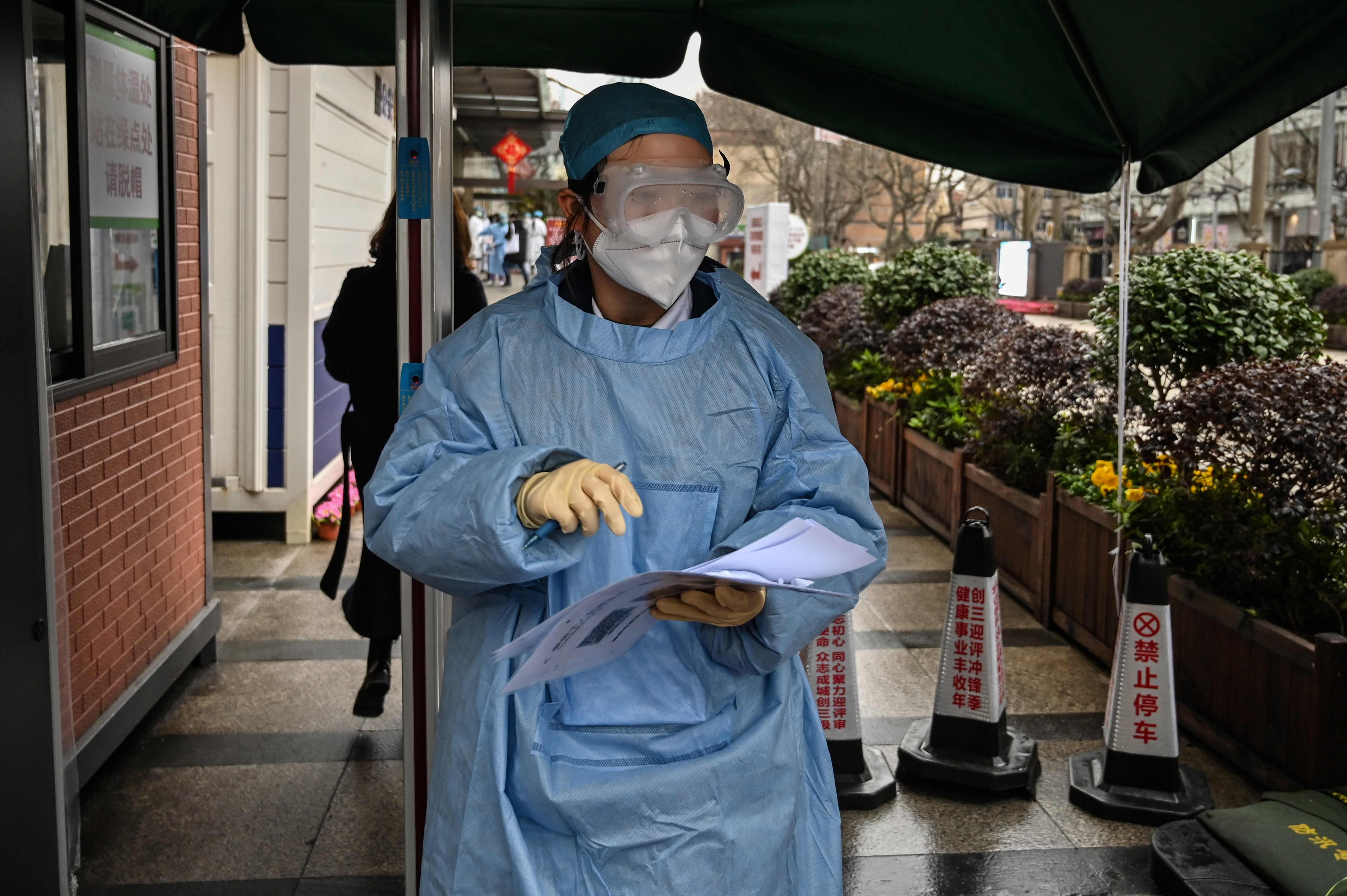 Seorang pekerja medis mengenakan pakaian pelindung berdiri di depan sebuah rumah sakit di Distrik Xuhui, Shanghai, Tiongkok.