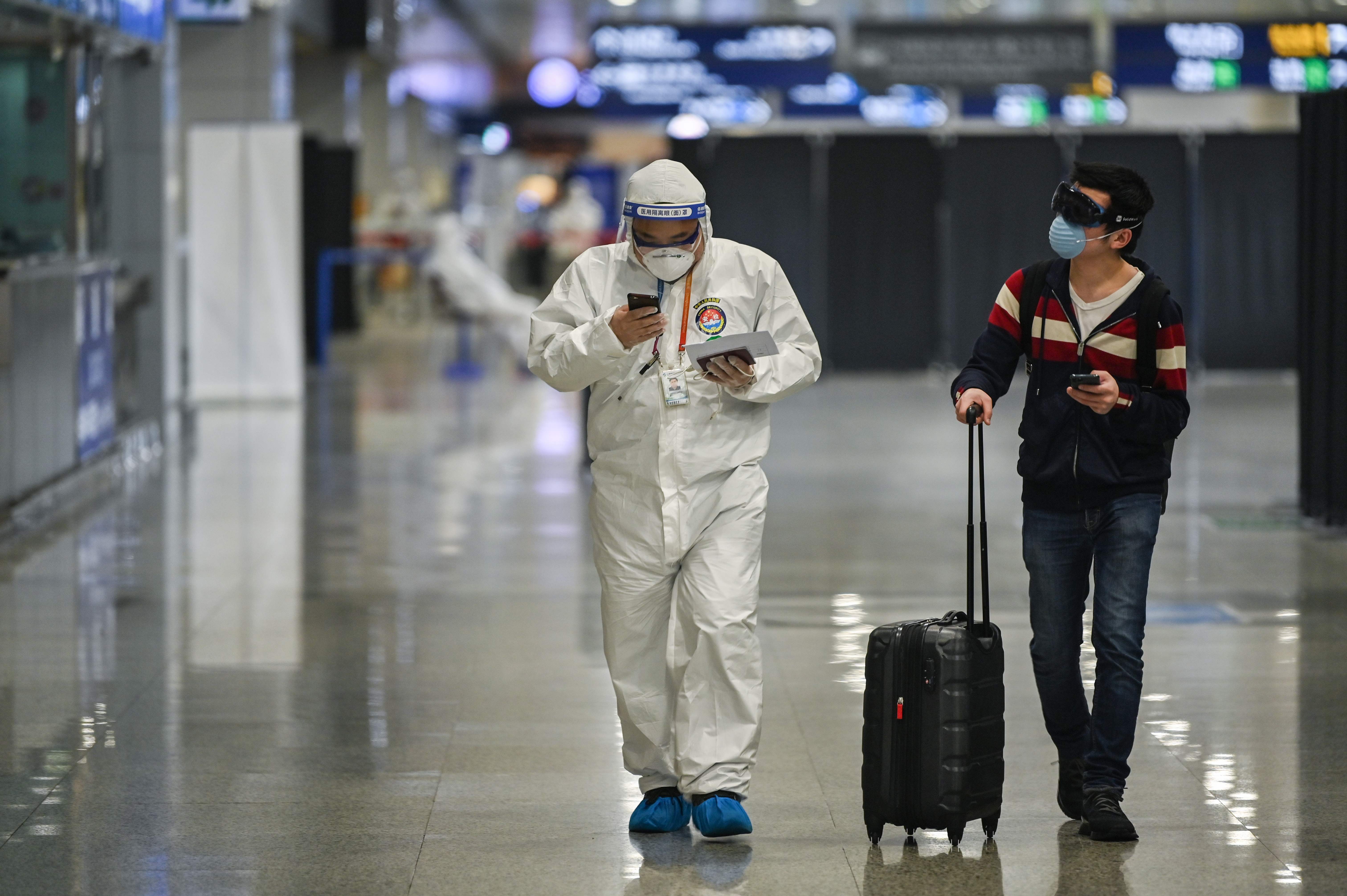 Seorang petugas kesehatan berpakaian pelindung berjalan dengan seorang penumpang yang tiba di Bandara Internasional Pudong, Shanghai.