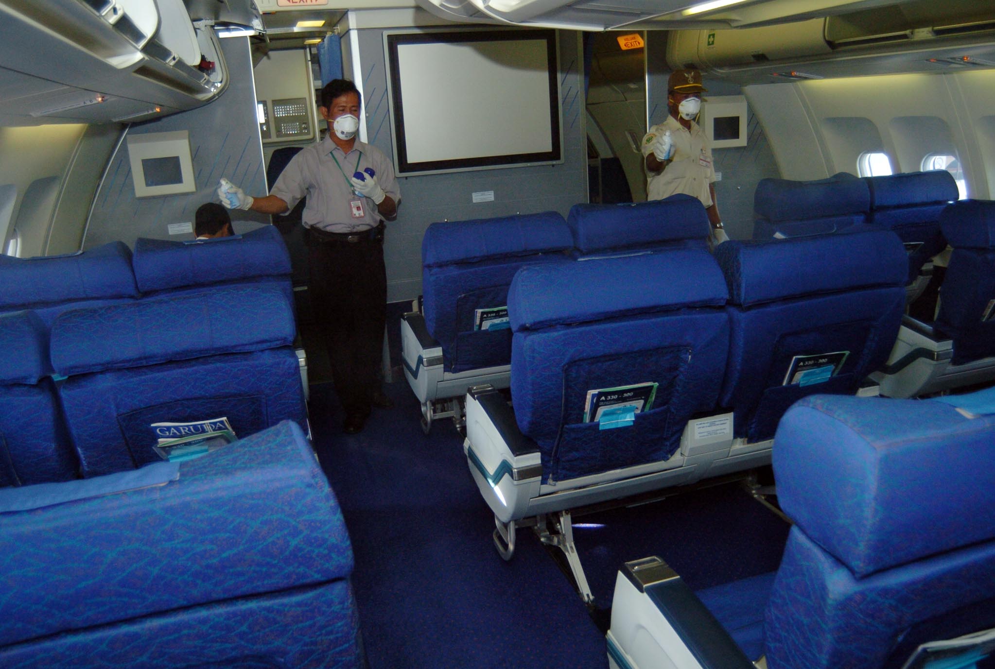 Dua petugas menyemprotkan cairan disinfektan ke ruangan kabin dan kursi penumpang pesawat Airbus 330 Garuda yang baru tiba dari Korea