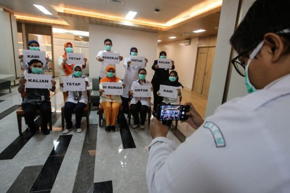 Petugas medis melakukan foto dengan memegang tulisan Kami Tetap Bekerja Untuk Kalian, Kalian Tetap di Rumah Untuk Kami di RSCM, Jakarta.
