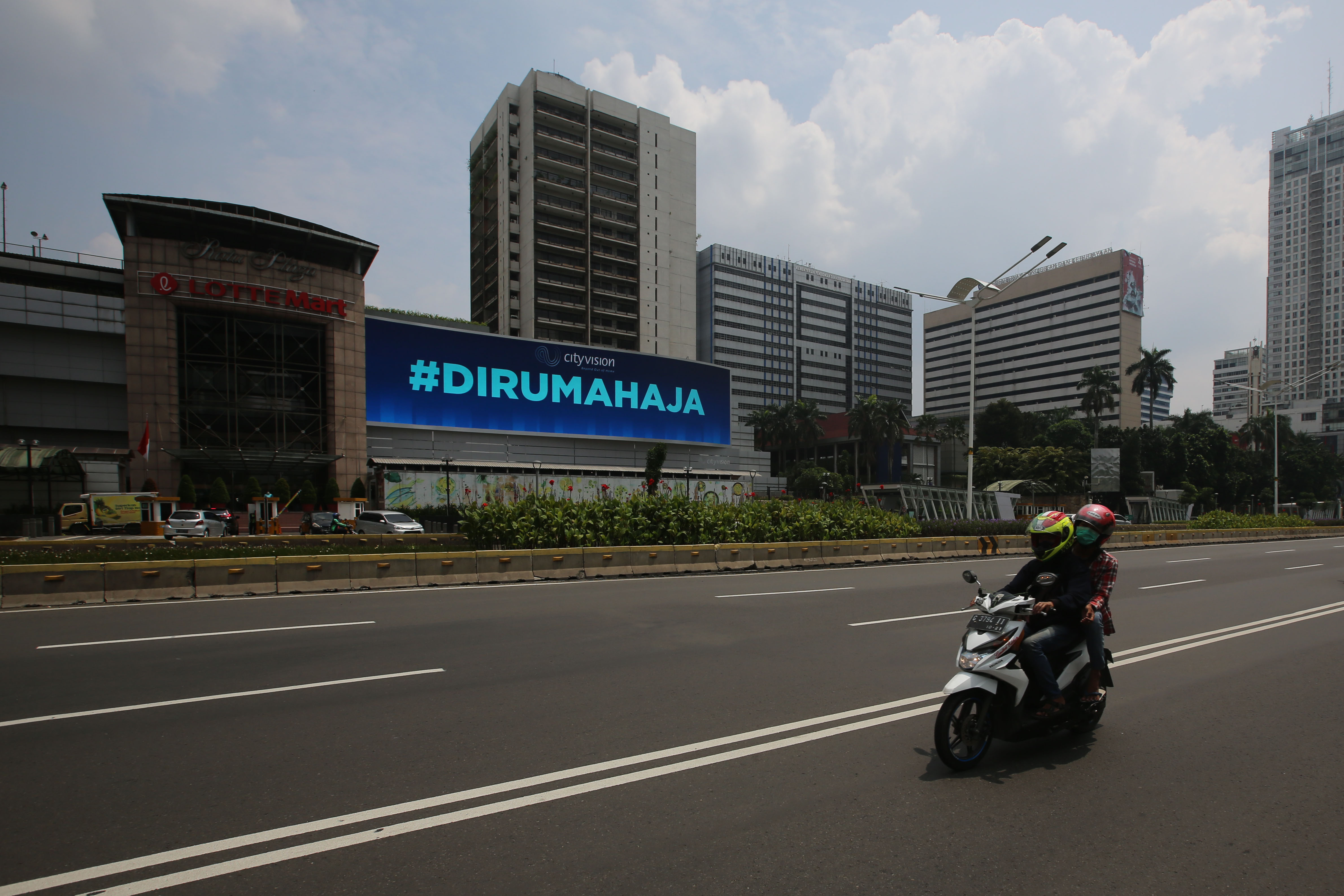 Pengendara melintasi papan iklan elektronik berbunyi imbauan #DIRUMAHAJA, sebagai upaya menekan penyebaran covid-19.