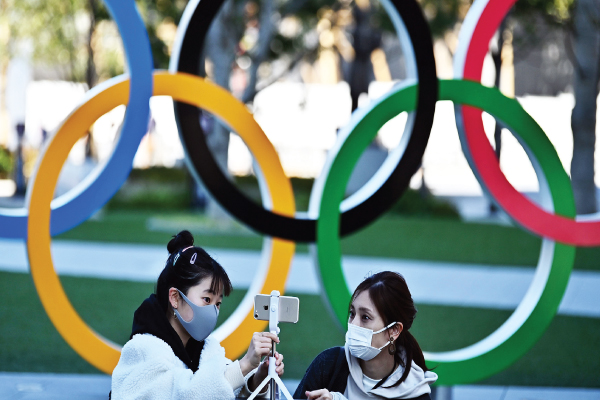 Sembari mengenakan masker, warga berfoto di instalasi lambang Olimpiade yang dipasang di Tokyo, Jepang, beberapa waktu lalu.