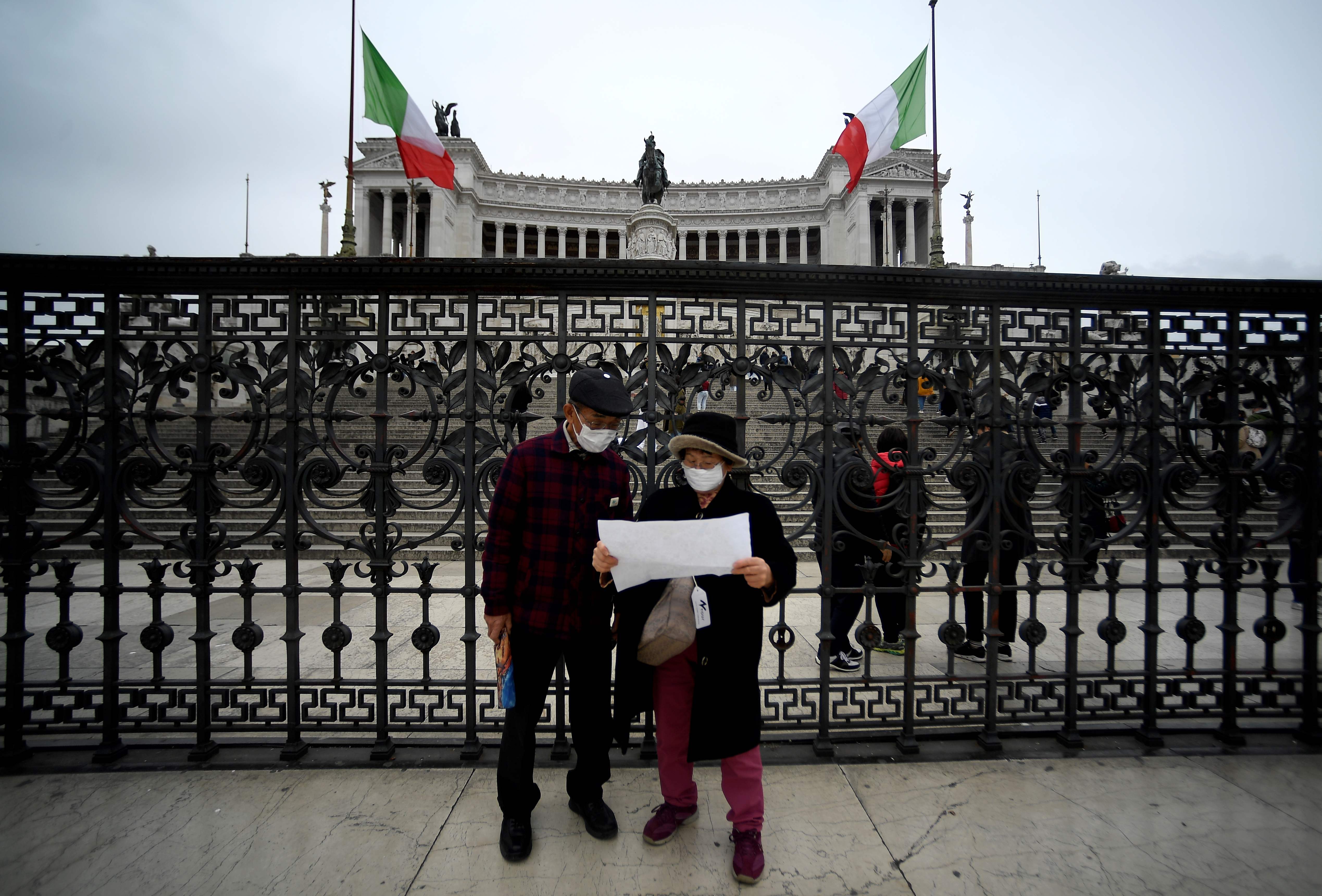 Turis mengenakan masker berdiri di depan Vittoriano di Roma, Italia.