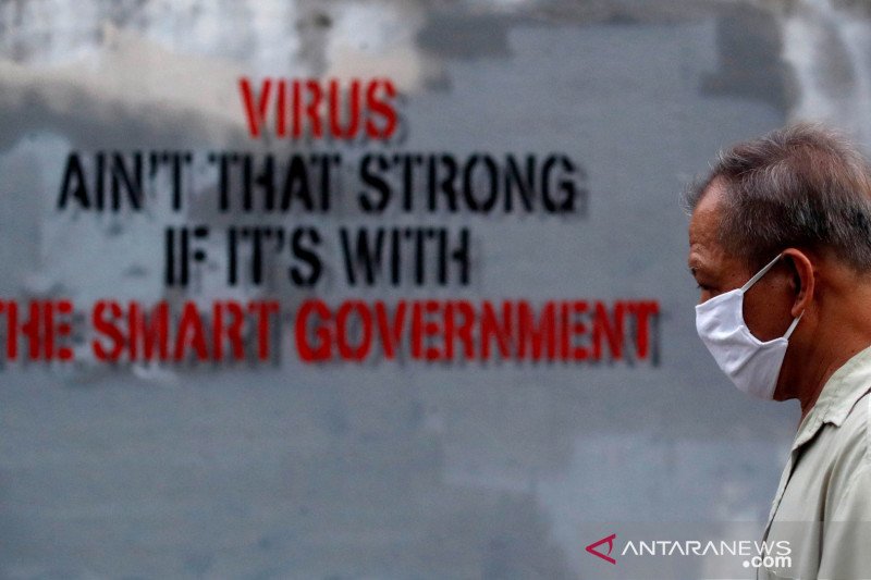 Seorang pria memakai masker saat berjalan melewati grafiti di tengah meluasnya penularan virus korona di Bangkok, Thailand.