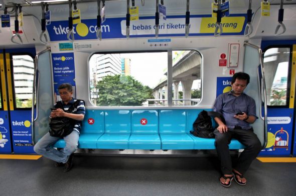 Pengguna MRT duduk dengan jarak tertentu yang sudah diatur dengan ditandai stiker saat melintasi kawasan Fatmawati, Jakarta.