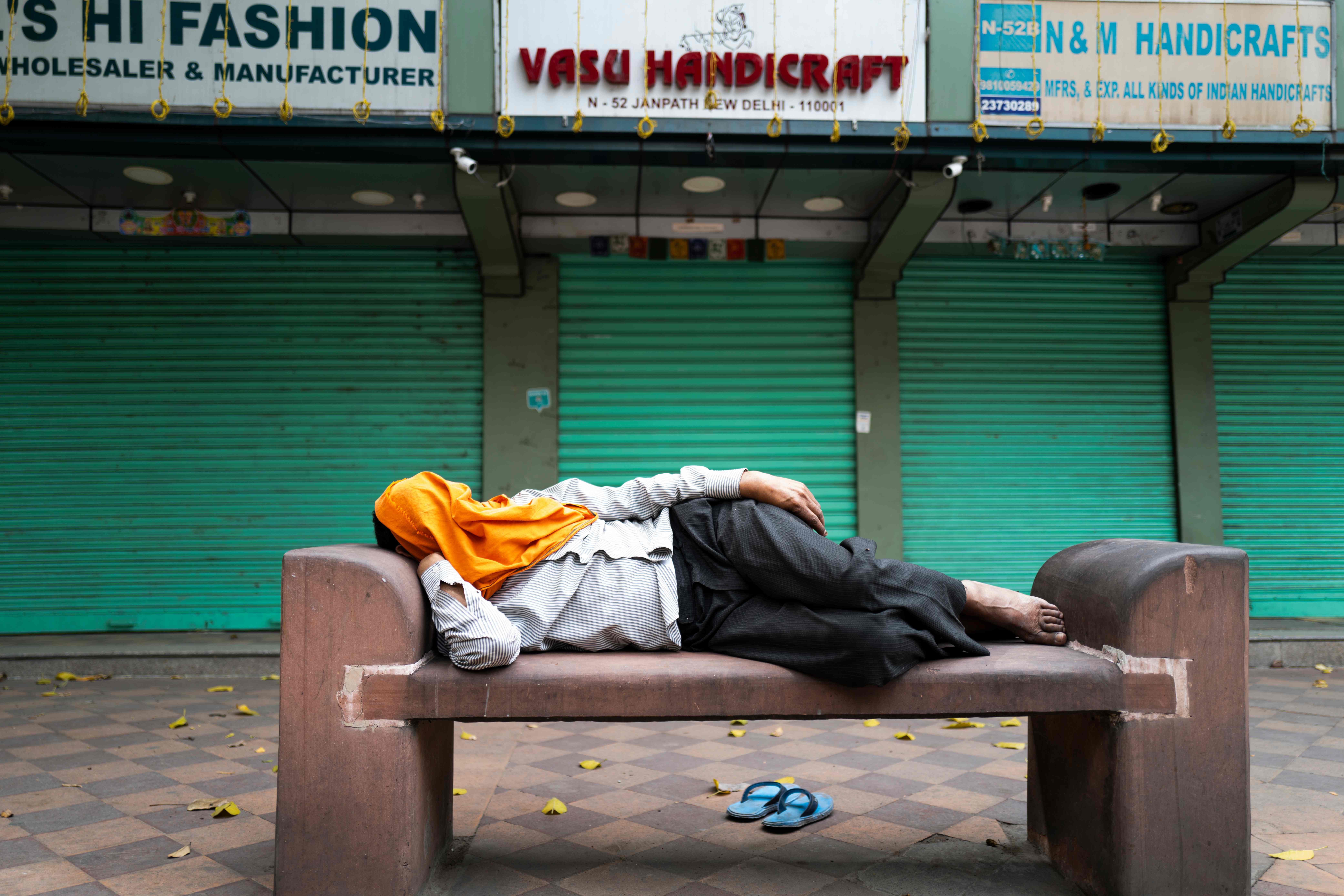 Seorang warga India tertidur di kursi umum di depan toko-toko yang tutup setelah negara itu melakukan kebijakan lockdown.