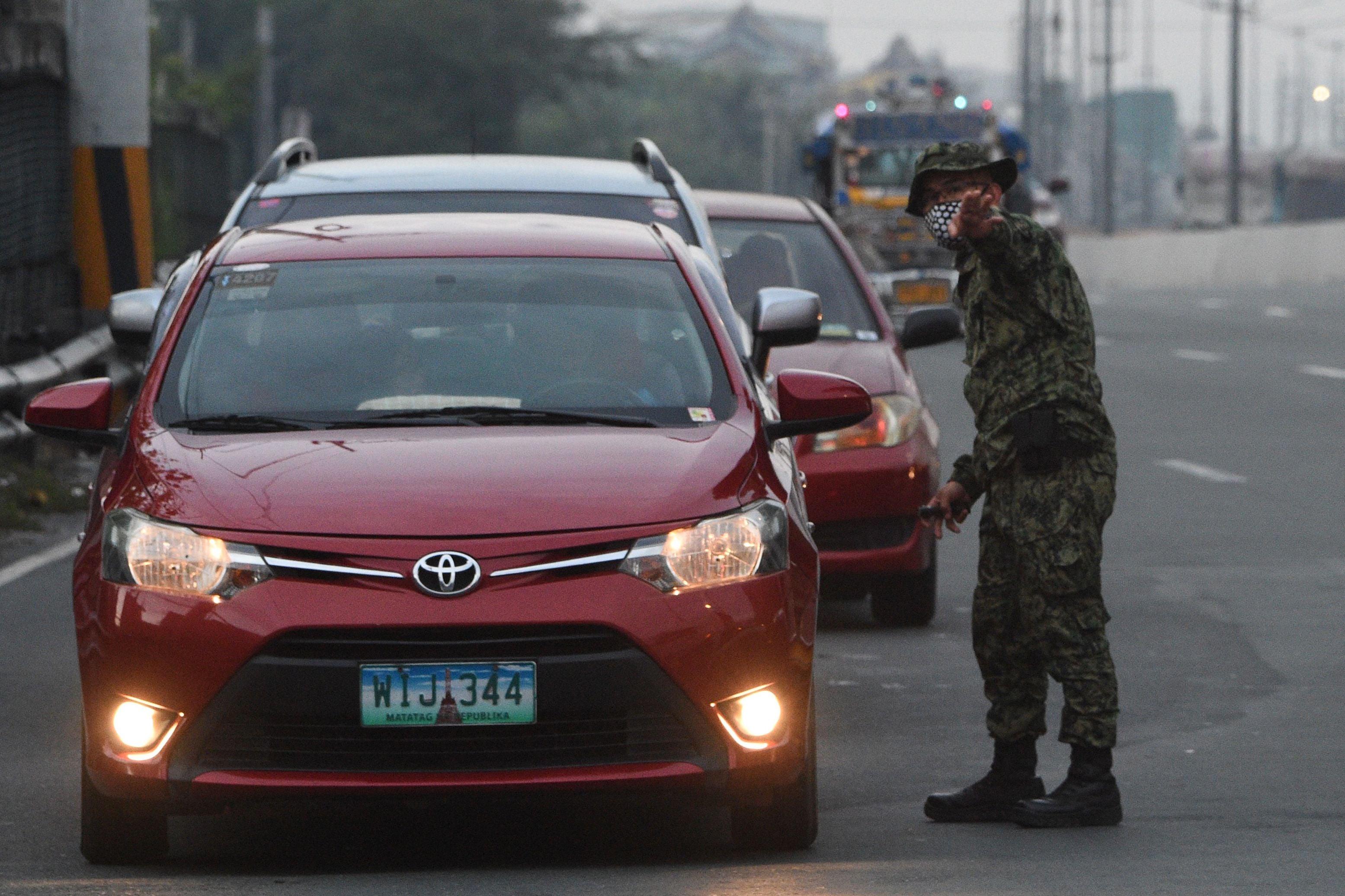 Seorang polisi Filipina memberikan petunjuk kepada pengemudi mobil di checkpoint di perbatasan Manila.