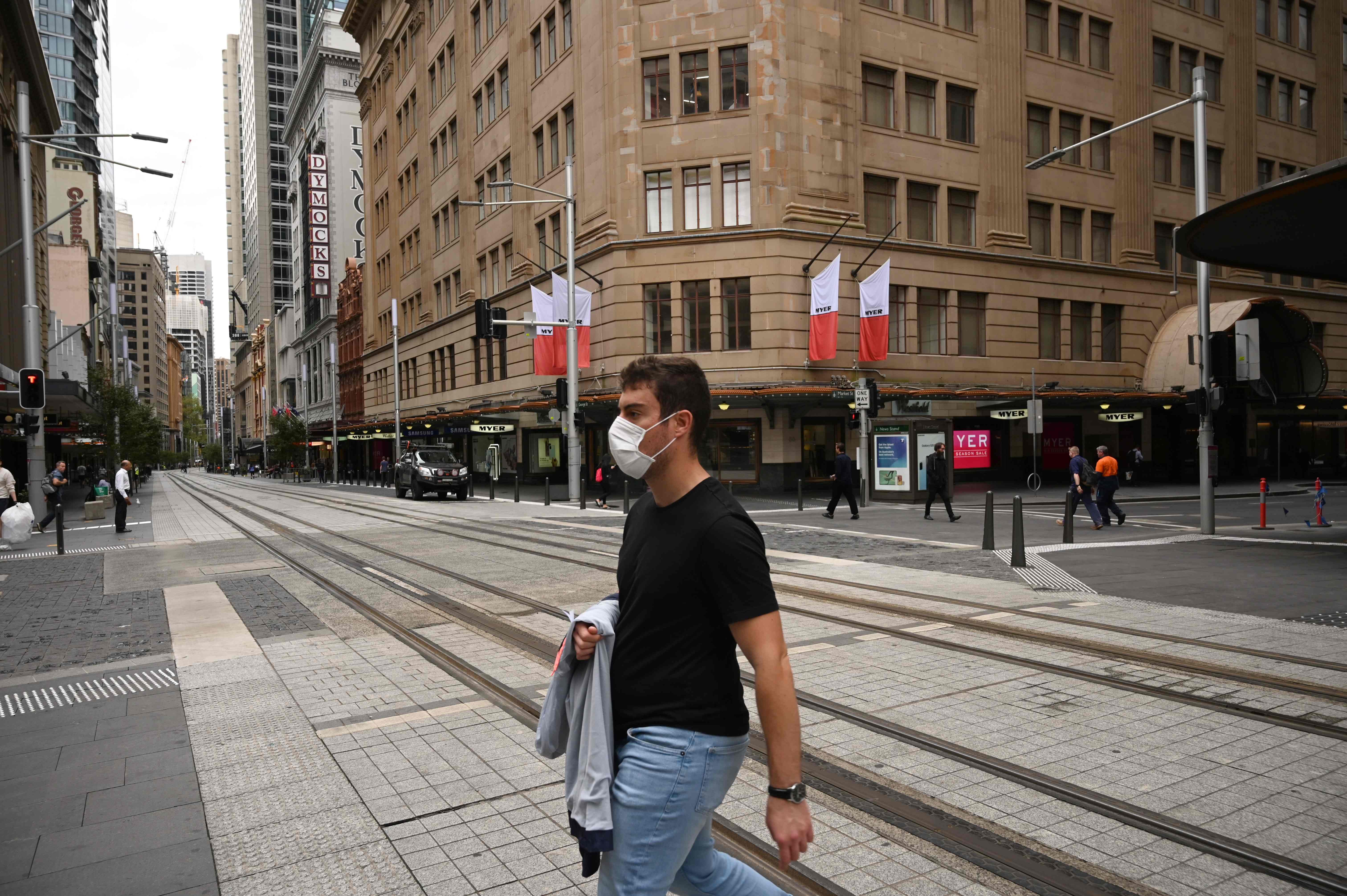 Seorang pria mengenakan masker berjalan di jalan kota Sydney, Australia yang kosong.