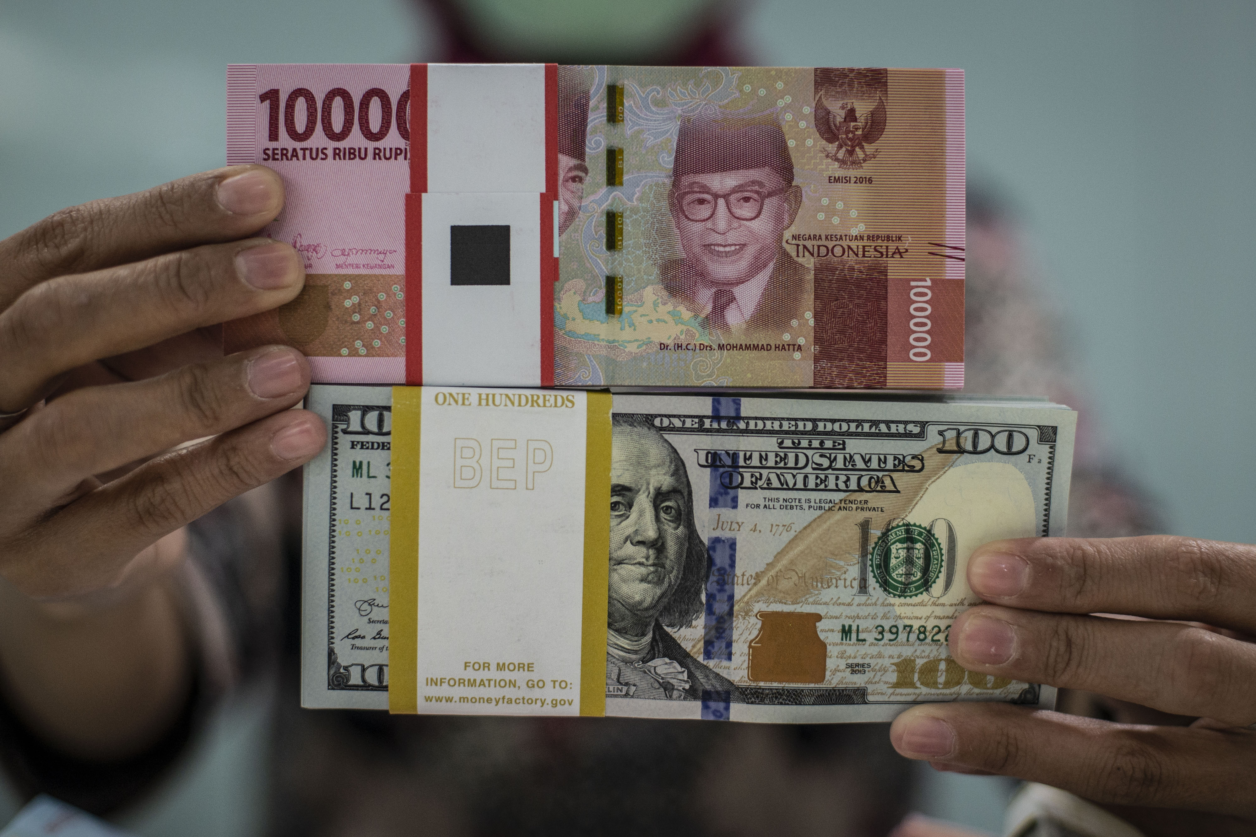 Karyawan bank menunjukkan uang rupiah dan dolar AS.