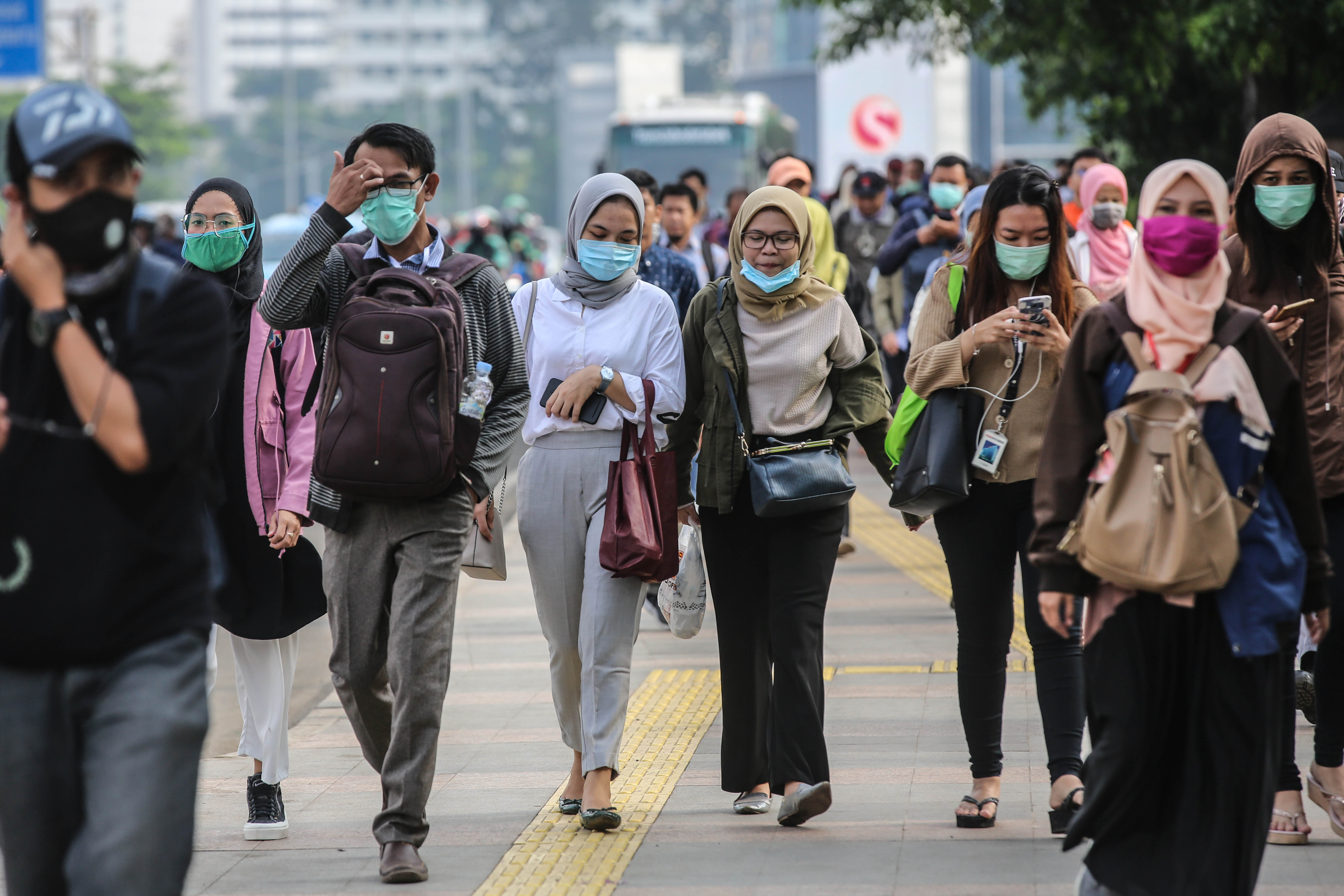  Pekerja kompak menggunakan masker pelindung saat melewati jalur pedestrian di kawasan Sudirman, Jakarta.