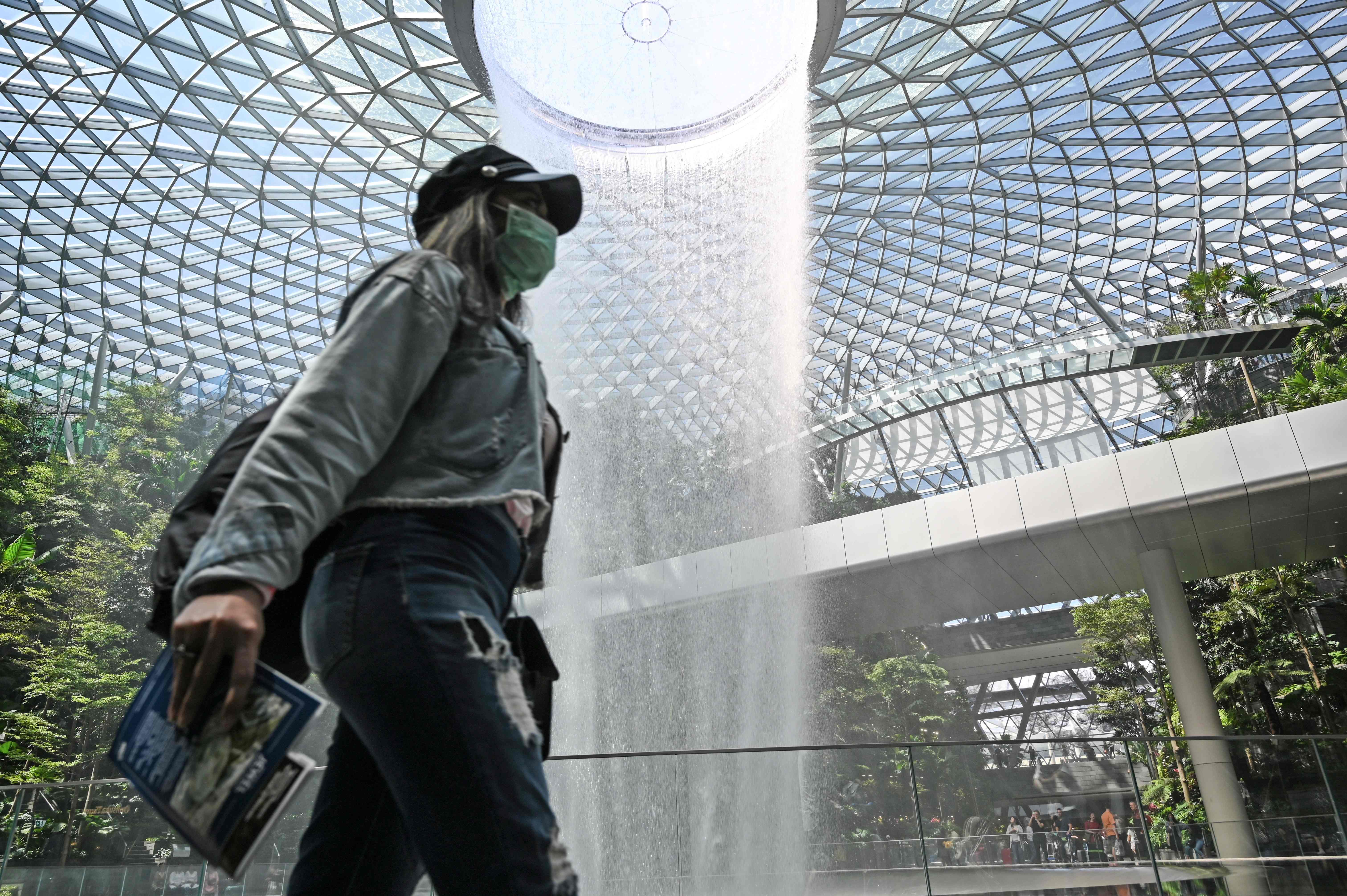 Seorang pelancong mengenakan masker saat melintas di depan Rain Vortex di Bandara Changi, Singapura.