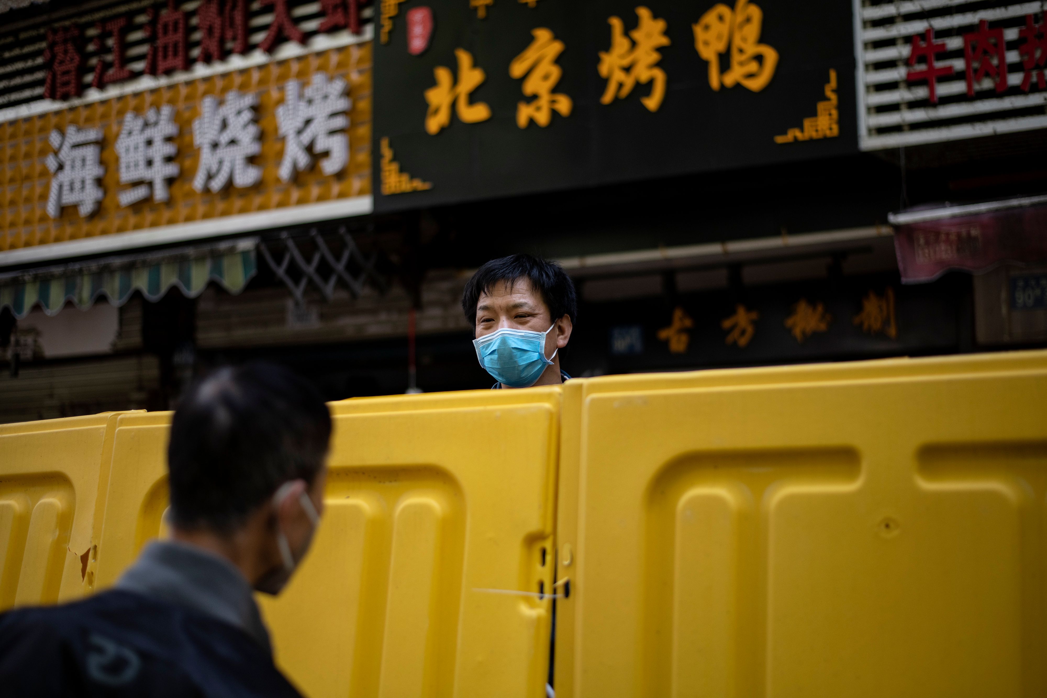 Seorang pria mengenakan masker berbicara dengan pria lainnya melewati barikade di Wuhan, Tiongkok