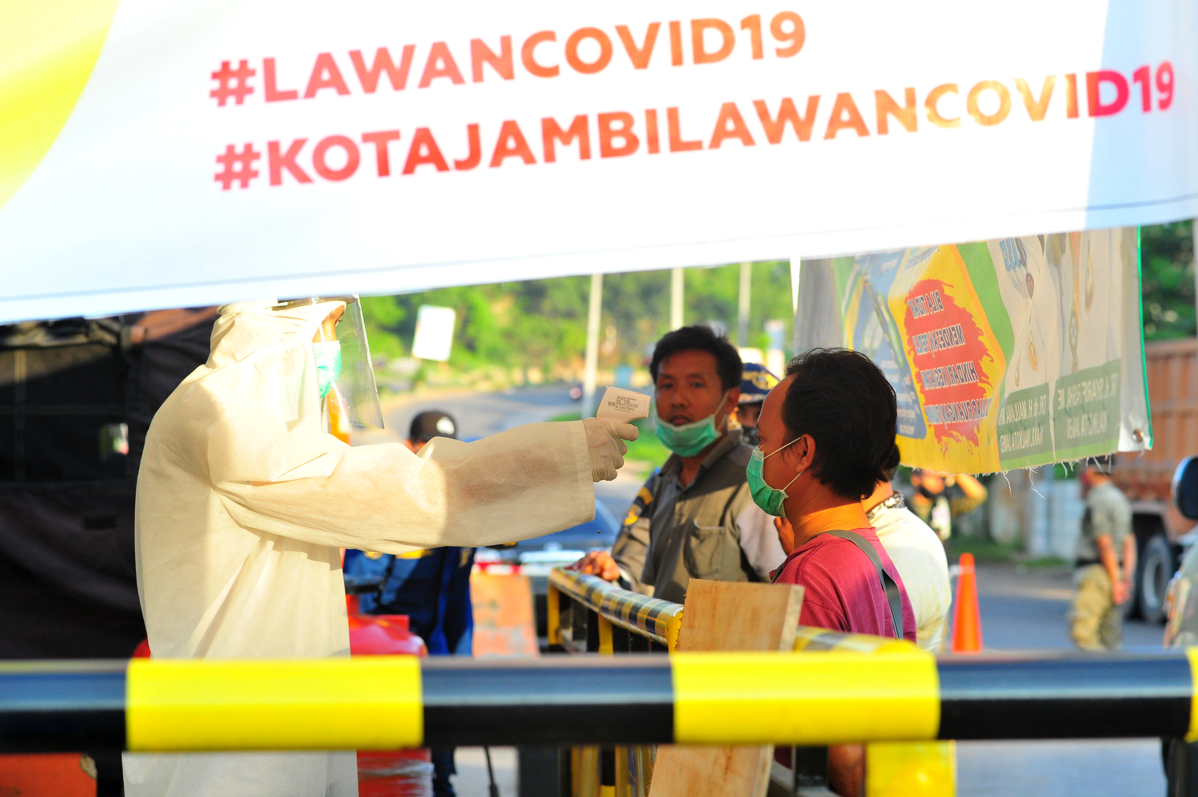 Petugas mengecek suhu warga yang akan memasuki Kota Jambi di perbatasan Kota Jambi dengan Kabupaten Muarojambi, Jambi, Sabtu (11/4). 