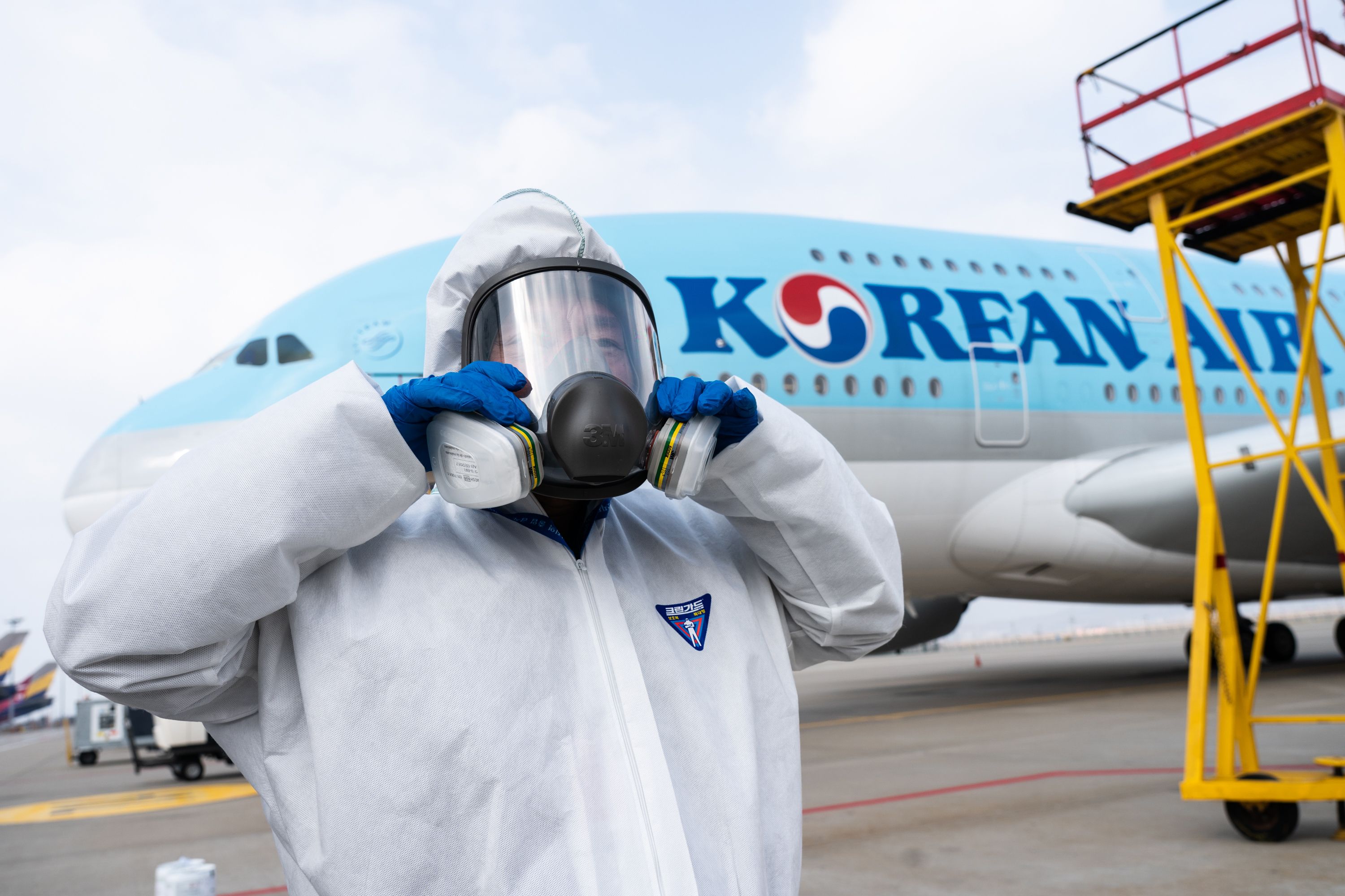 Seorang pekerja mengenakan APD sebelum menyemprotkan disinfektan di dalam pesawat milik Korean Air.