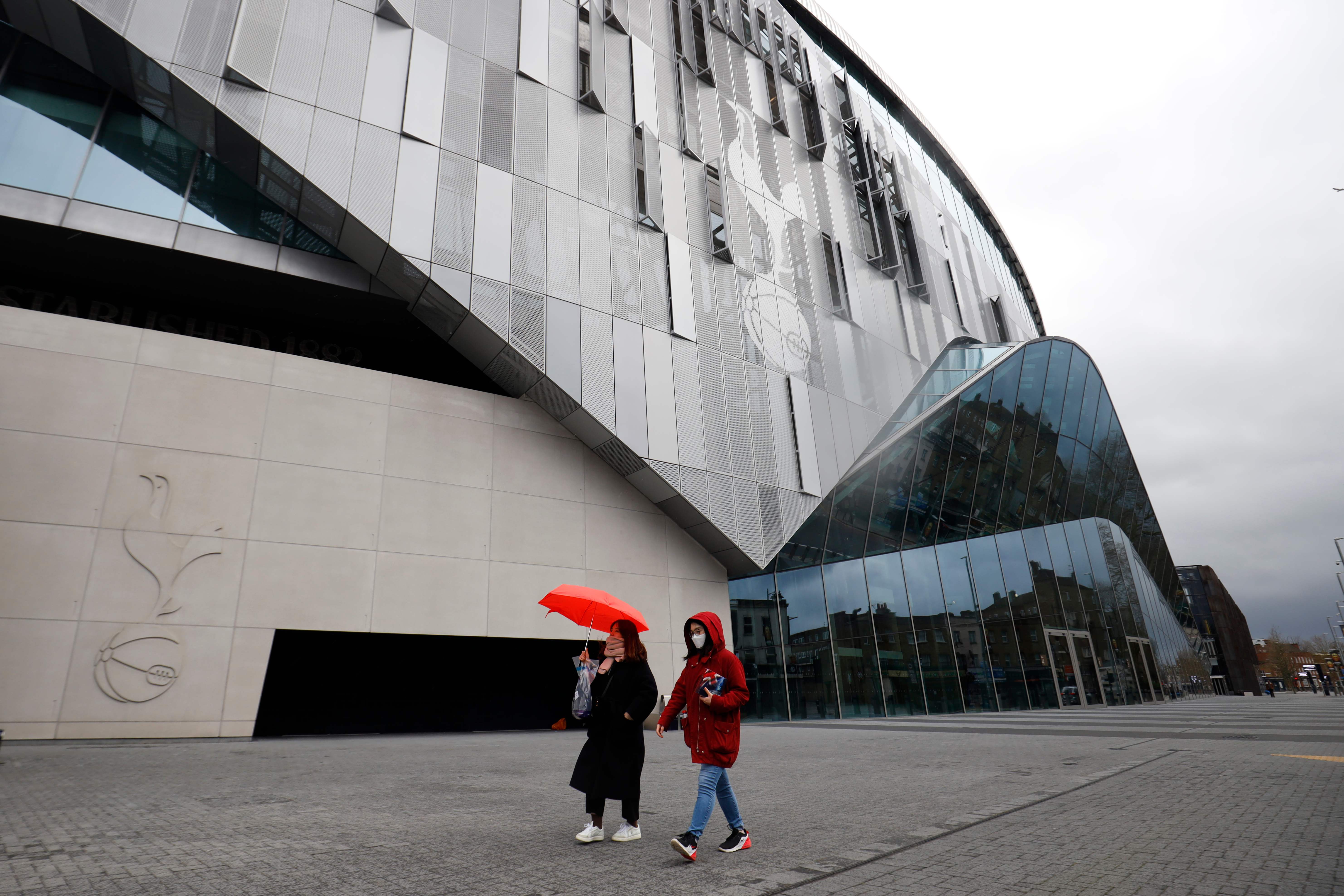 Dua orang berjalan di depan Stadion Tottenham Hotspur, London. Sejak wabah korona, Liga Inggris dihentikan dan gaji pemain dipotong.