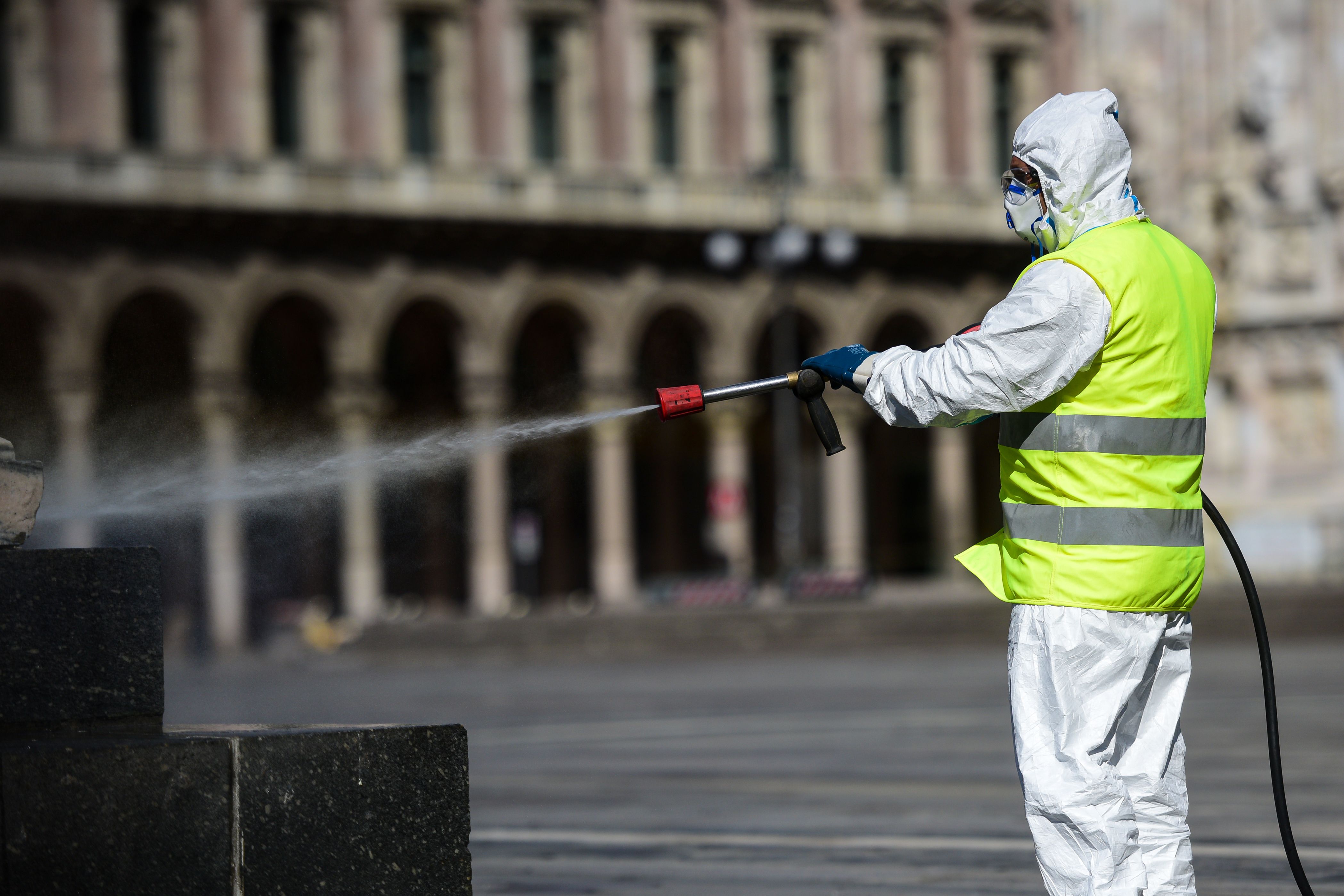 Seorang petugas menyemprotkan cairan disinfektan di Piazza Duomo, Milan, Italia.