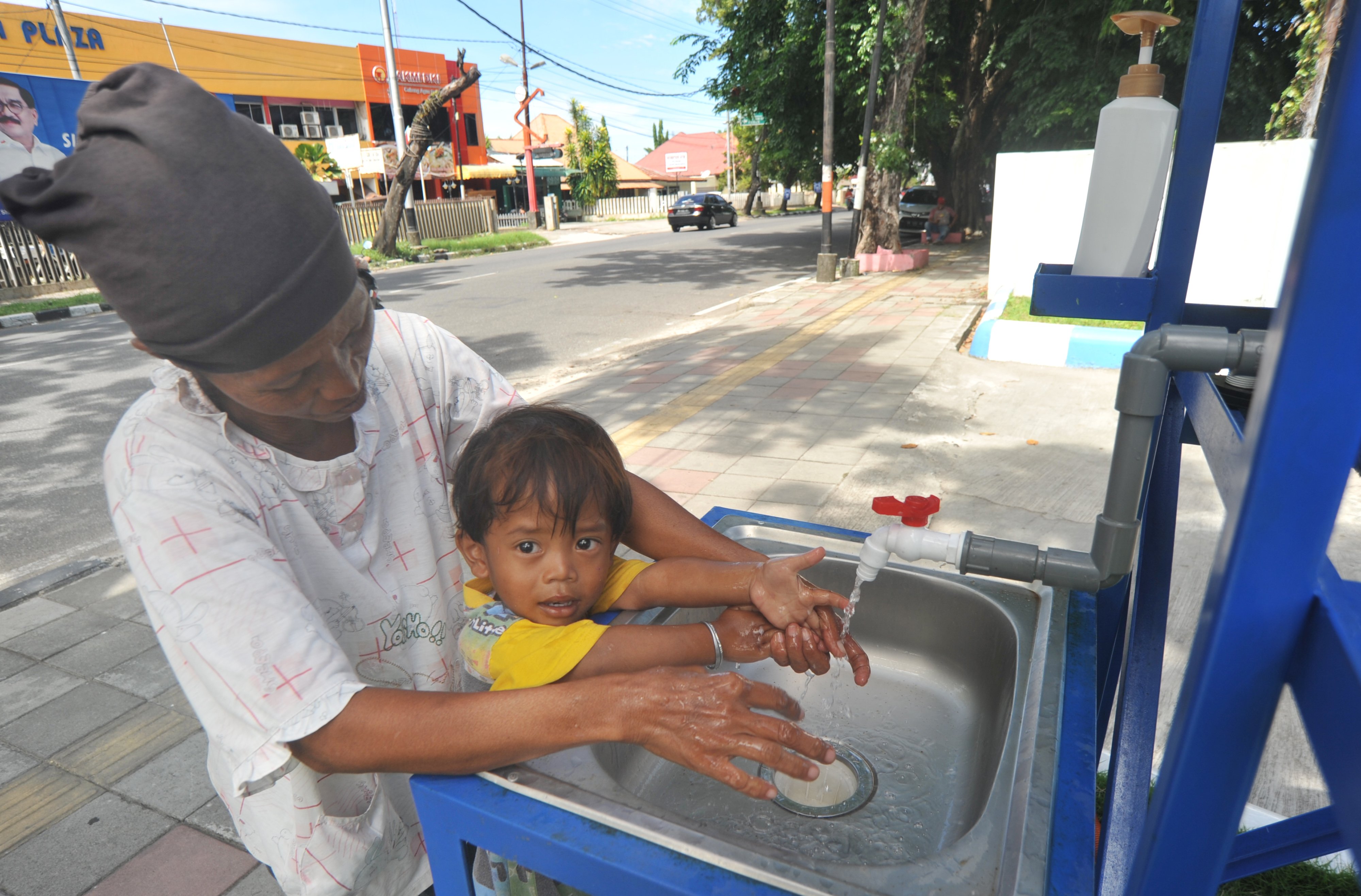 Warga bersama anaknya mencuci tangan di fasilitas cuci tangan gratis di Jl Agus Salim, Padang, Sumatera Barat, Jumat (3/4/2020