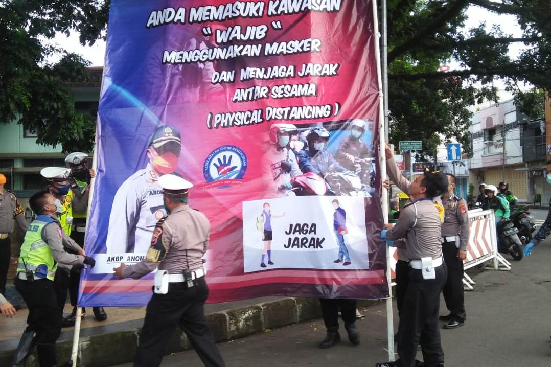 Petugas kepolisian memasang spanduk terkait physicial distancing.