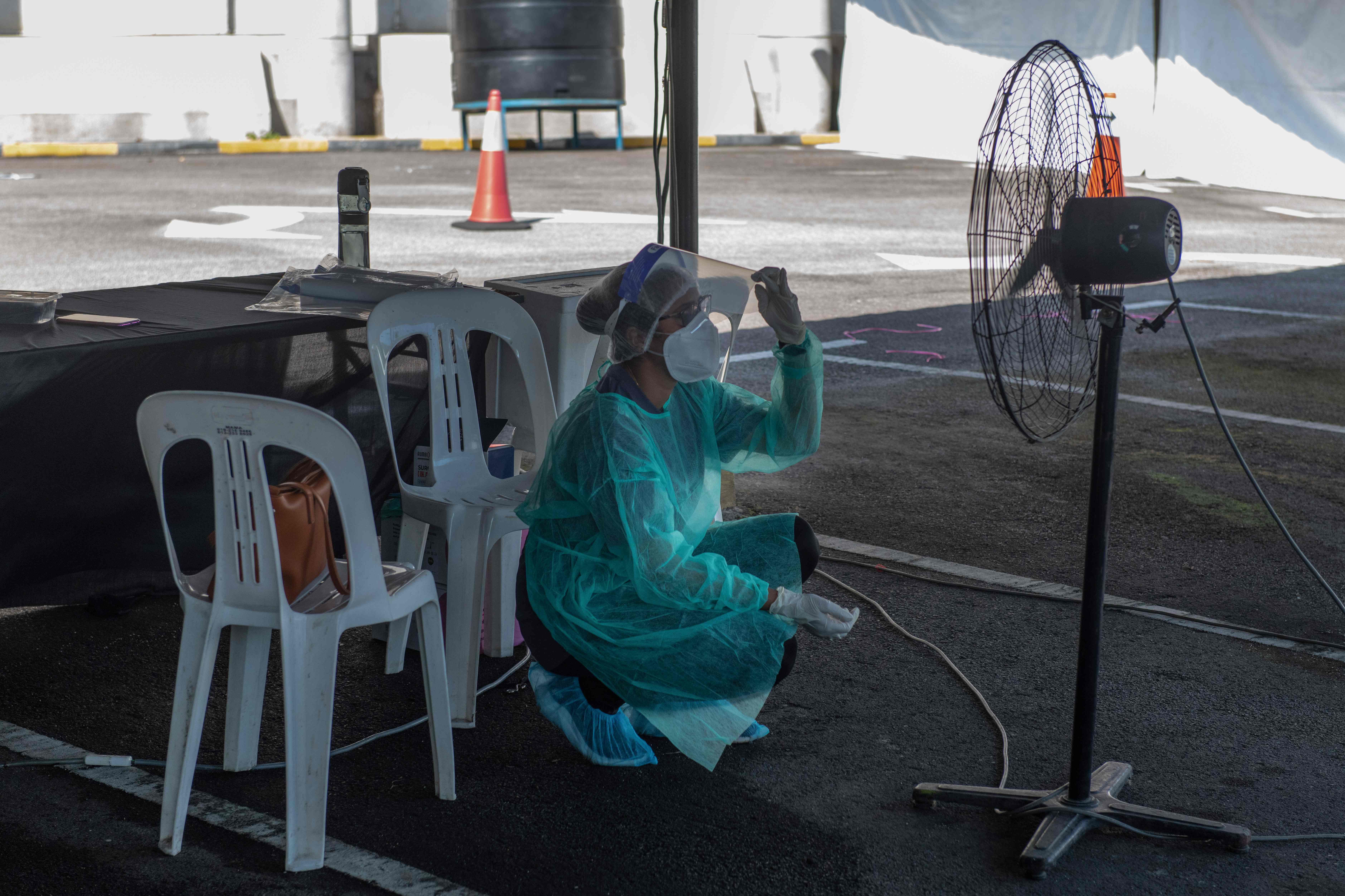 Seorang pekerja medis mendinginkan diri di depan kipas angin setelah mengambil sampel covid-19 di Kuala Lumpur, Malaysia.