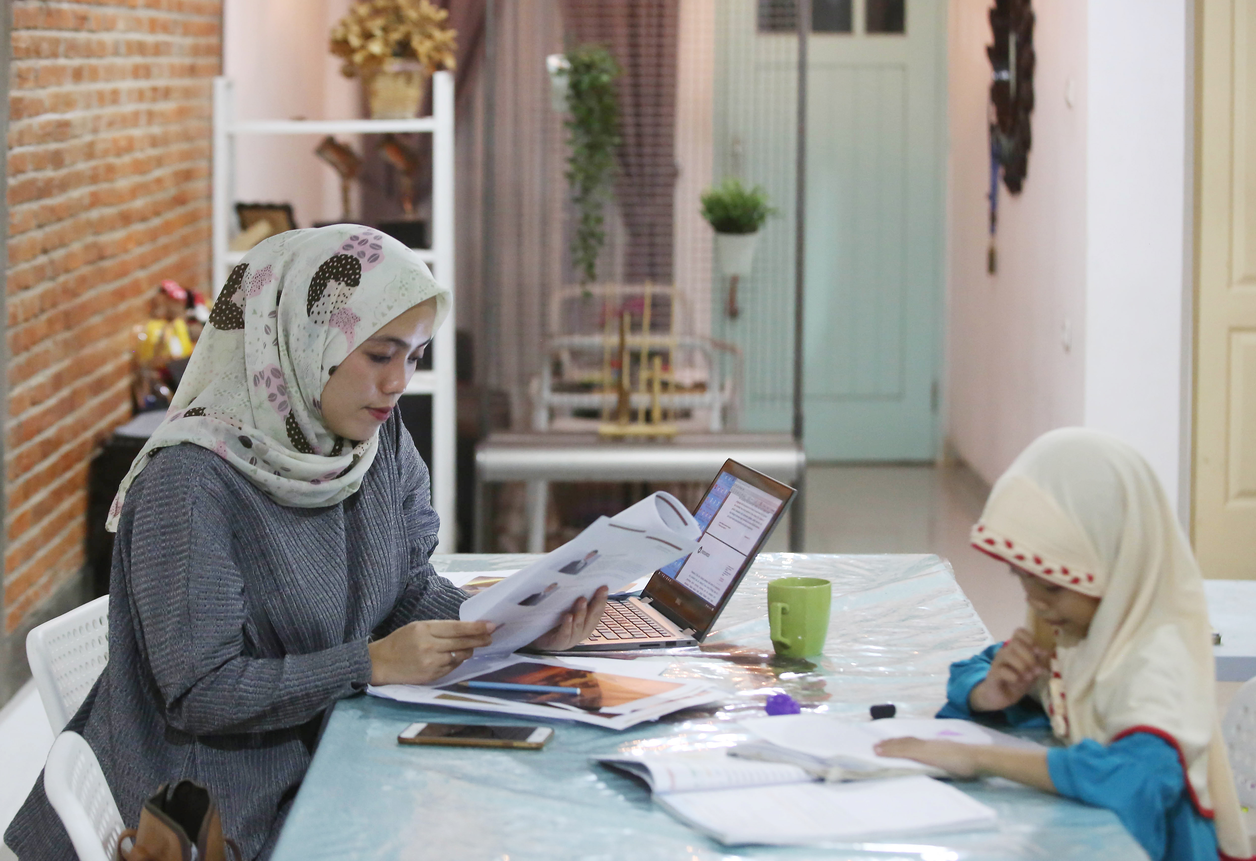 Afika, karyawan swasta, menyelesaikan pekerjaan sembari menemani anaknya yang belajar di rumah, di Jakarta.