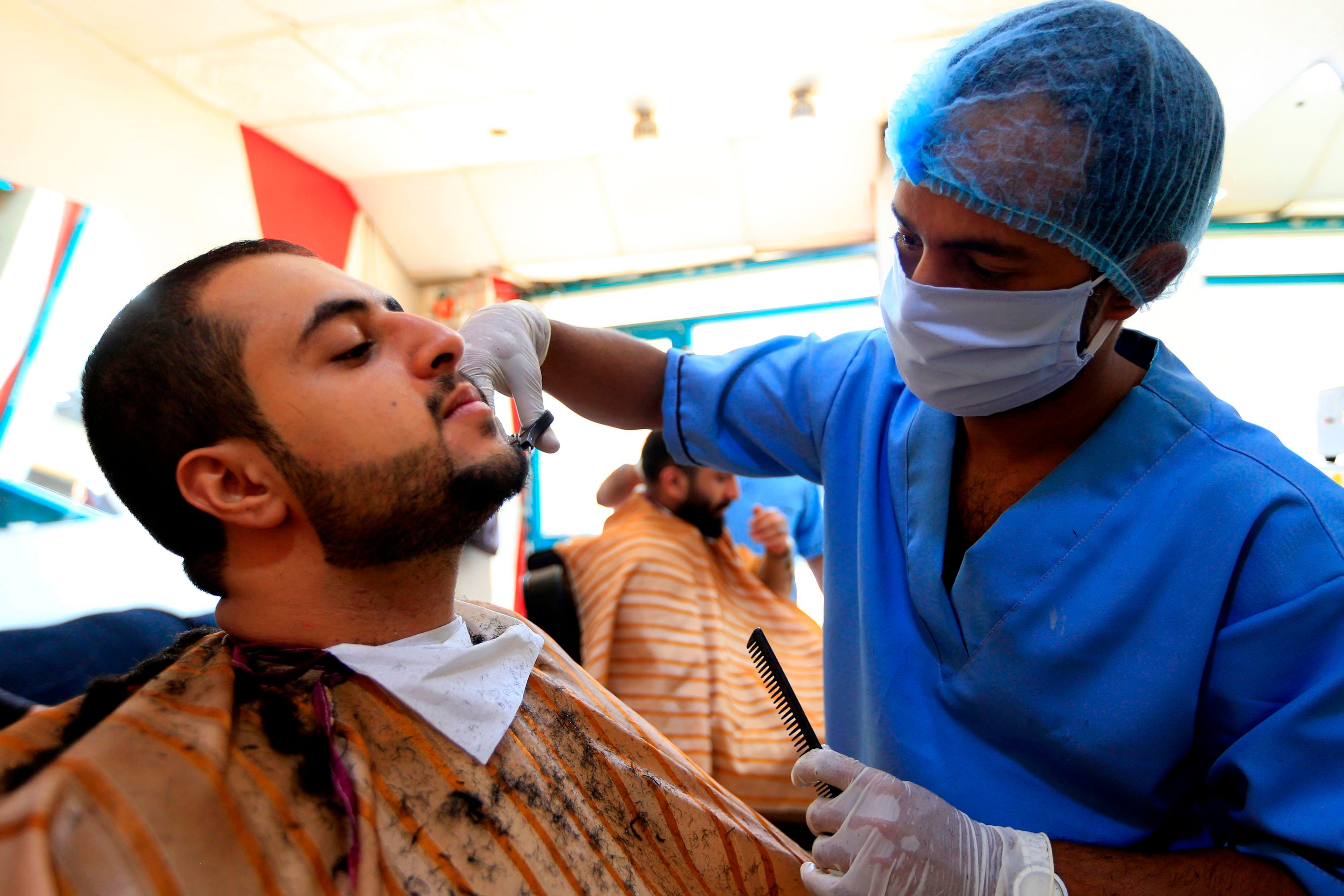 Tukang cukur mengenakan masker dan sarung tangan saat melayani pelanggannya di Sanaa. Yaman.
