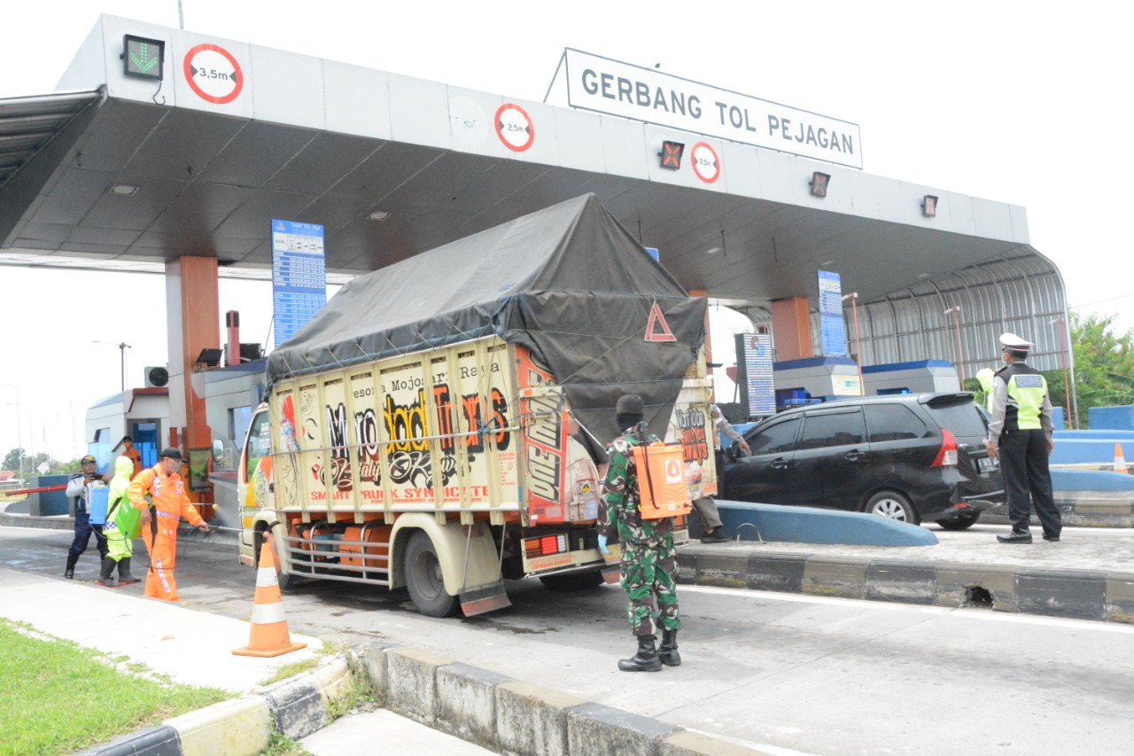 Seorang TNI menyemprot cairan disinfektan ke truk yang keluar dari pintu Tol Pejagan, Kamis (16/4/2020).