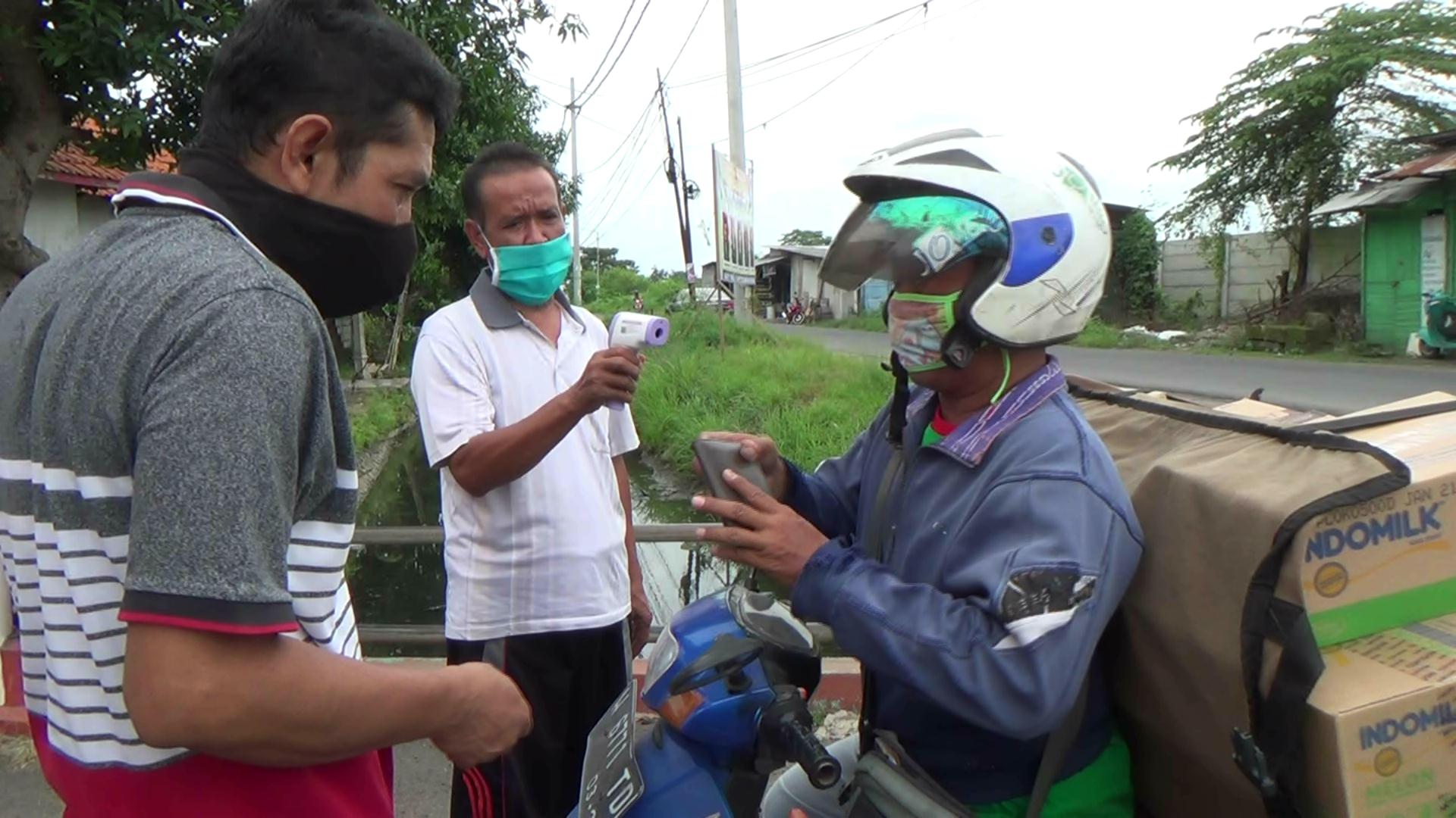 Warga melakukan pengecekan suhu tubuh terhadap seorang kurir barang.