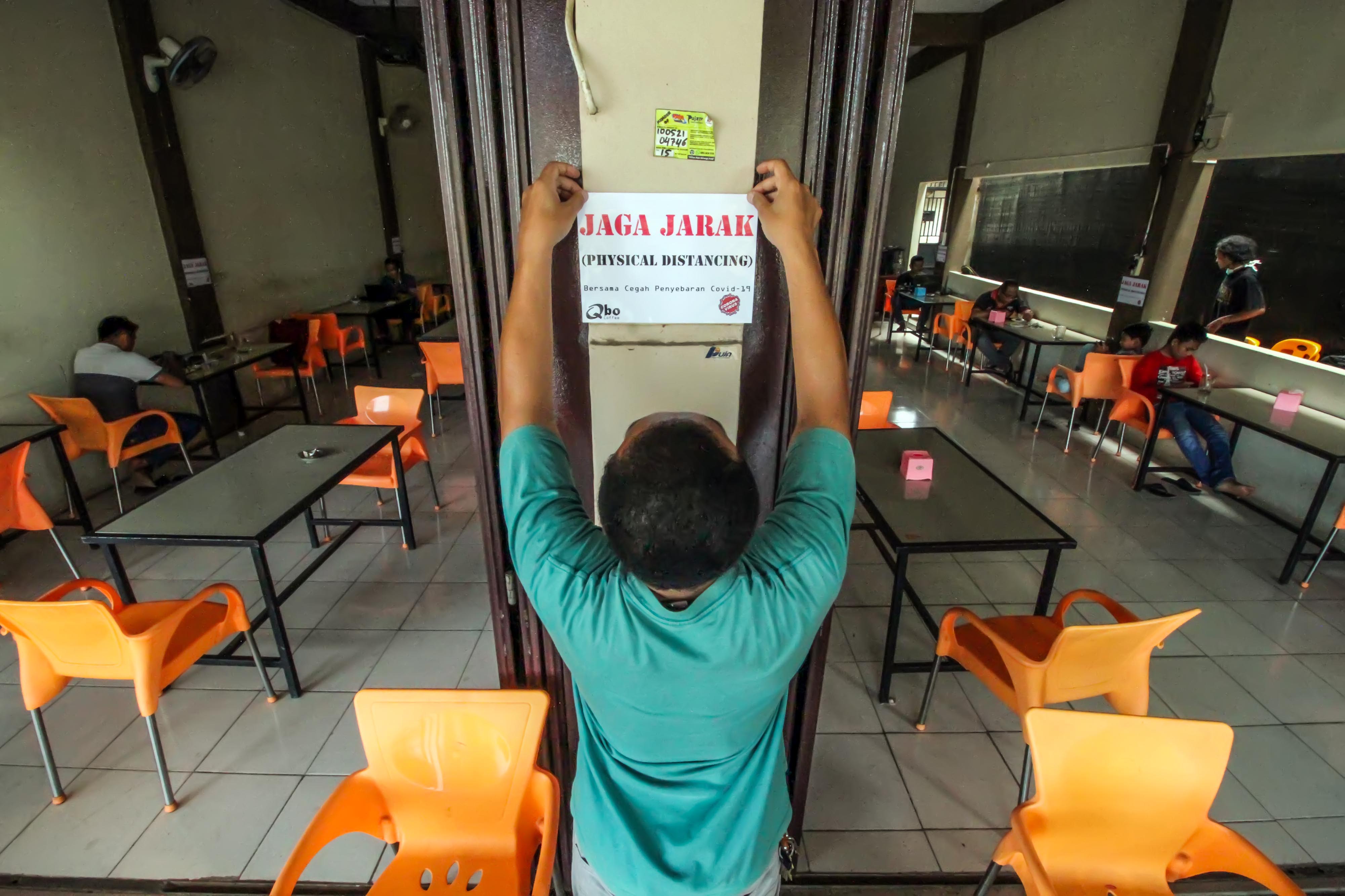 Pemilik warung kopi di Lhokseumawe, Aceh, menempelkan peringatan terkait physical distancing untuk mencegah penyebaran covid-19.