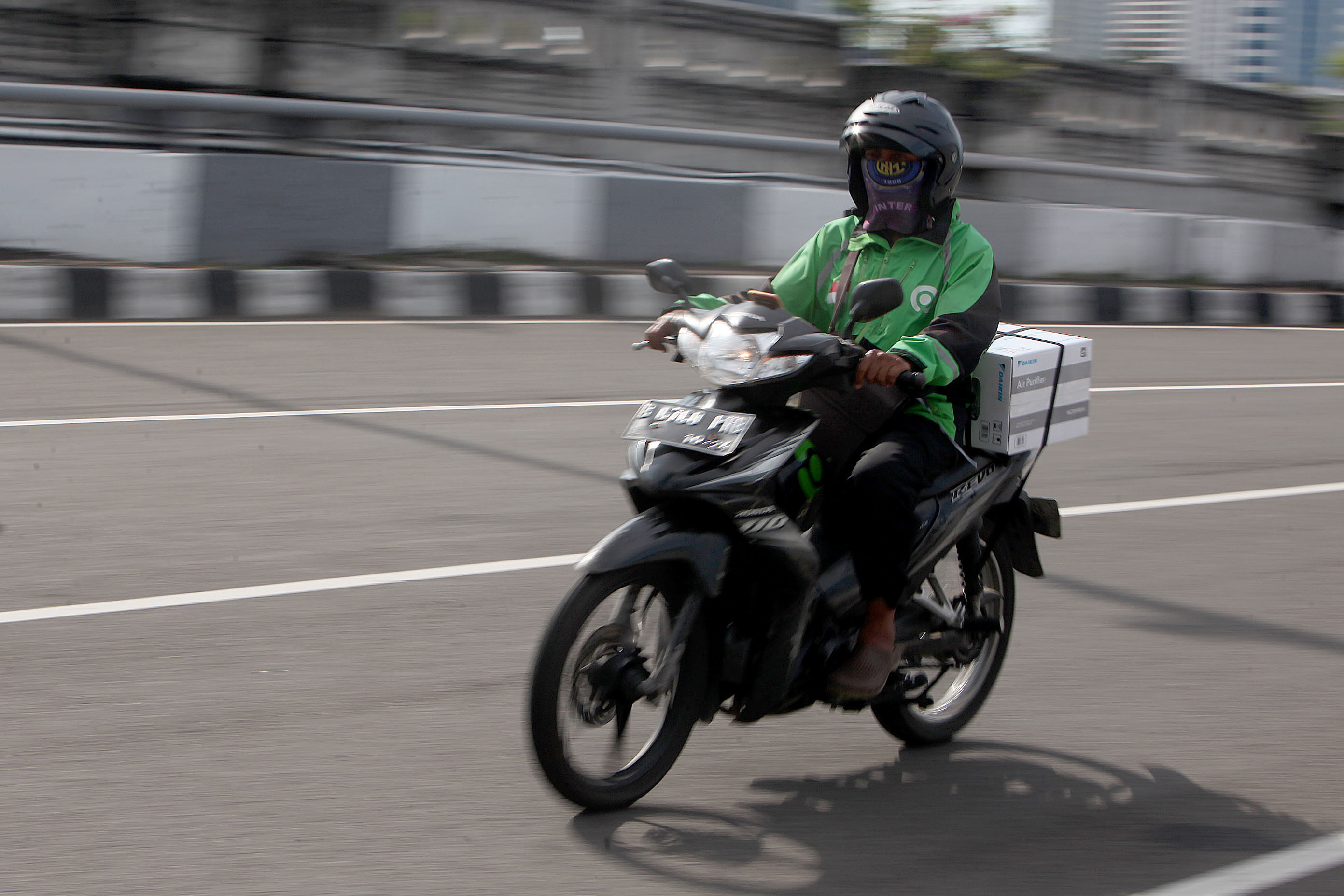 Pengendara ojek daring membawa paket saat melintas di kawasan Rasuna Said, Jakarta