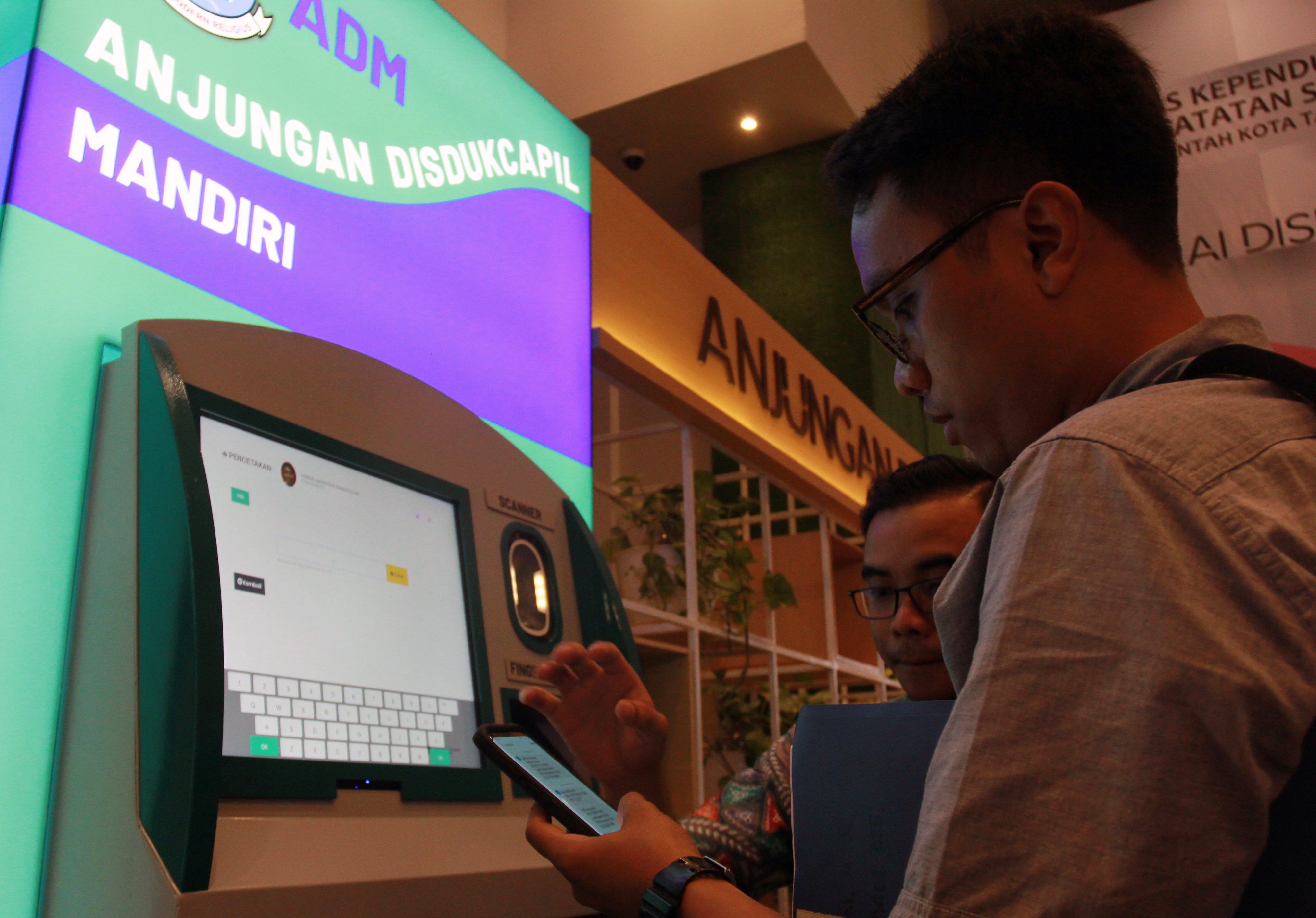 Warga dibantu petugas  Disdukcapil melakukan pencetakan KTP El di mesin Anjungan Dukcapil Mandiri di Serpong, Tangerang Selatan.