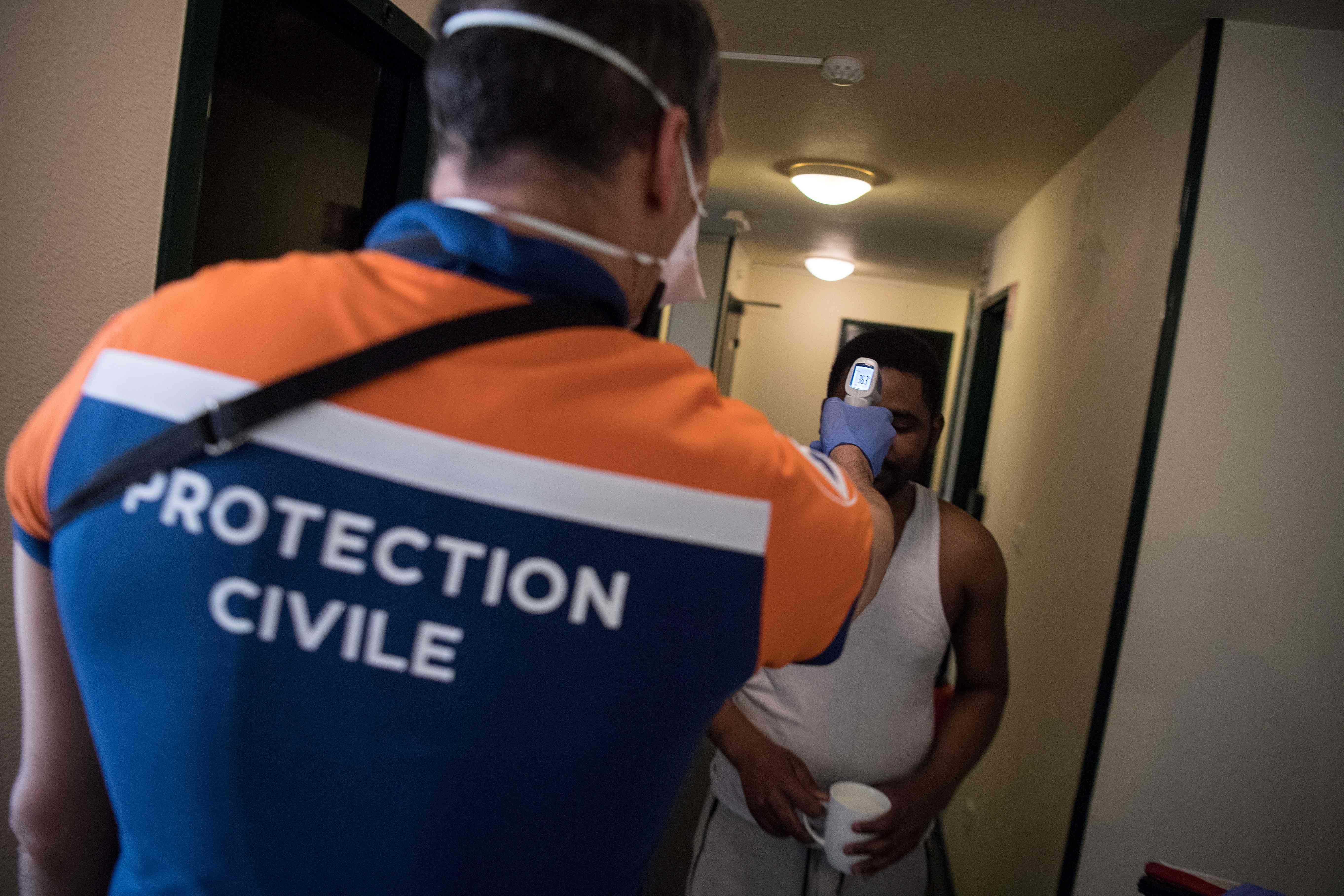 Anggota perlindungan sipil Prancis memeriksa suhu tubuh seorang imigran yang dikarantina di sebuah hotel di Nantes, Prancis.