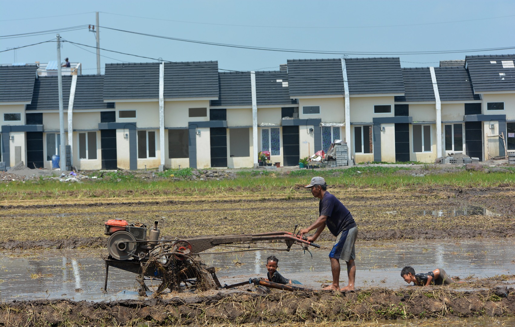 Buruh tani membajak sawah menggunakan traktor dengan latar belakang perumahan di areal persawahan di Jombang, Jawa Timur, Kamis (16/4).