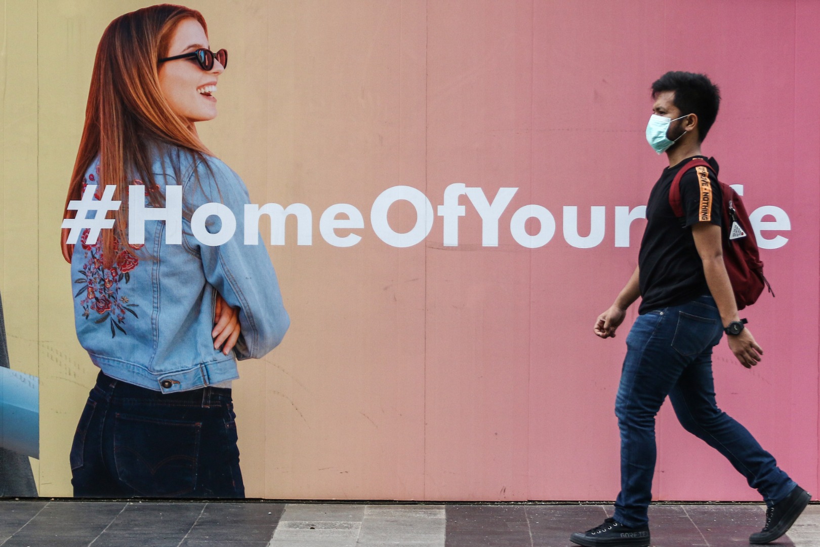 Pejalan kaki menggunakan masker melintasi trotoar di Jalan Jenderal Sudirman, Jakarta.